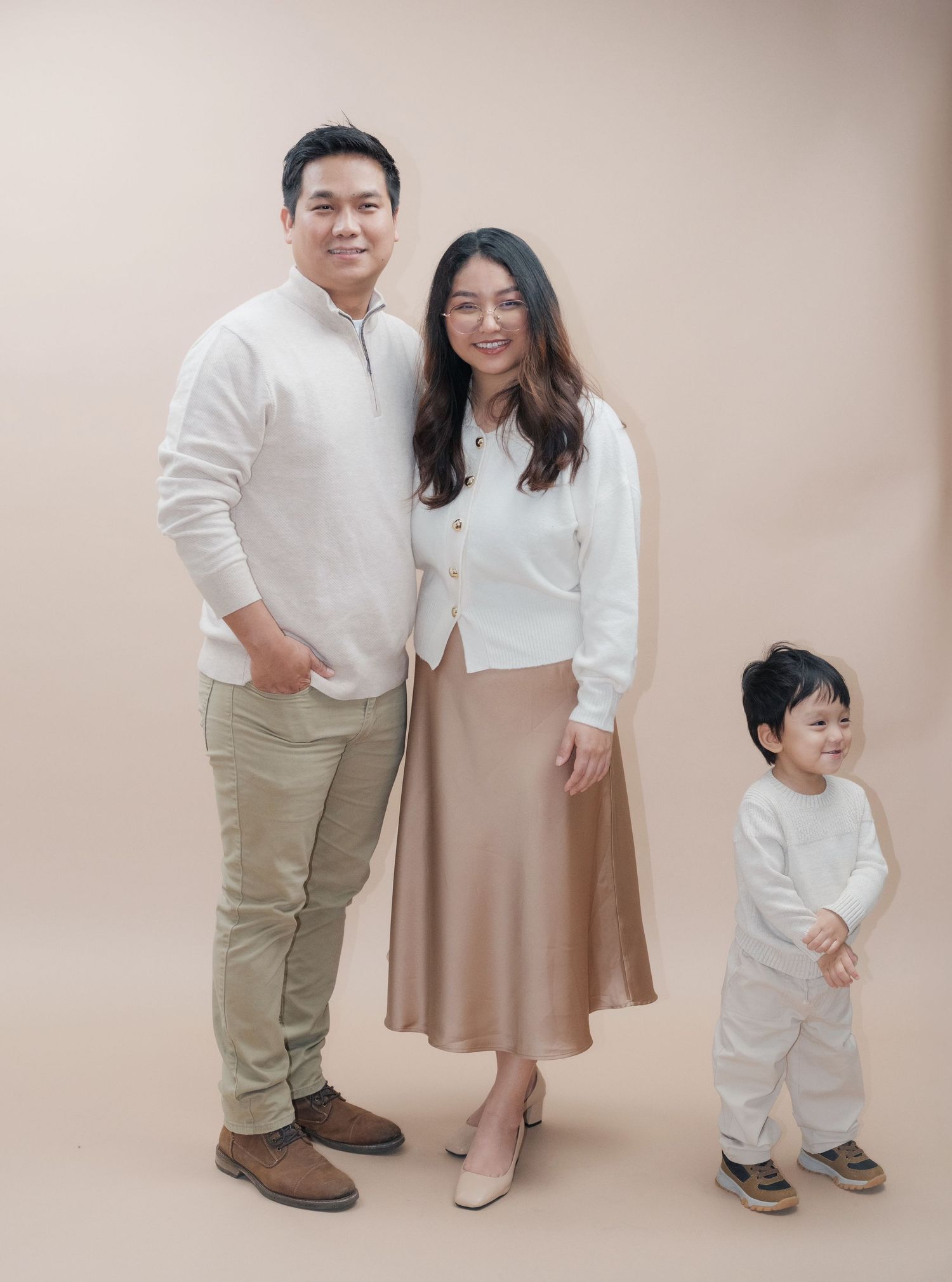 Family in coordinated neutral tones poses casually during portrait session.