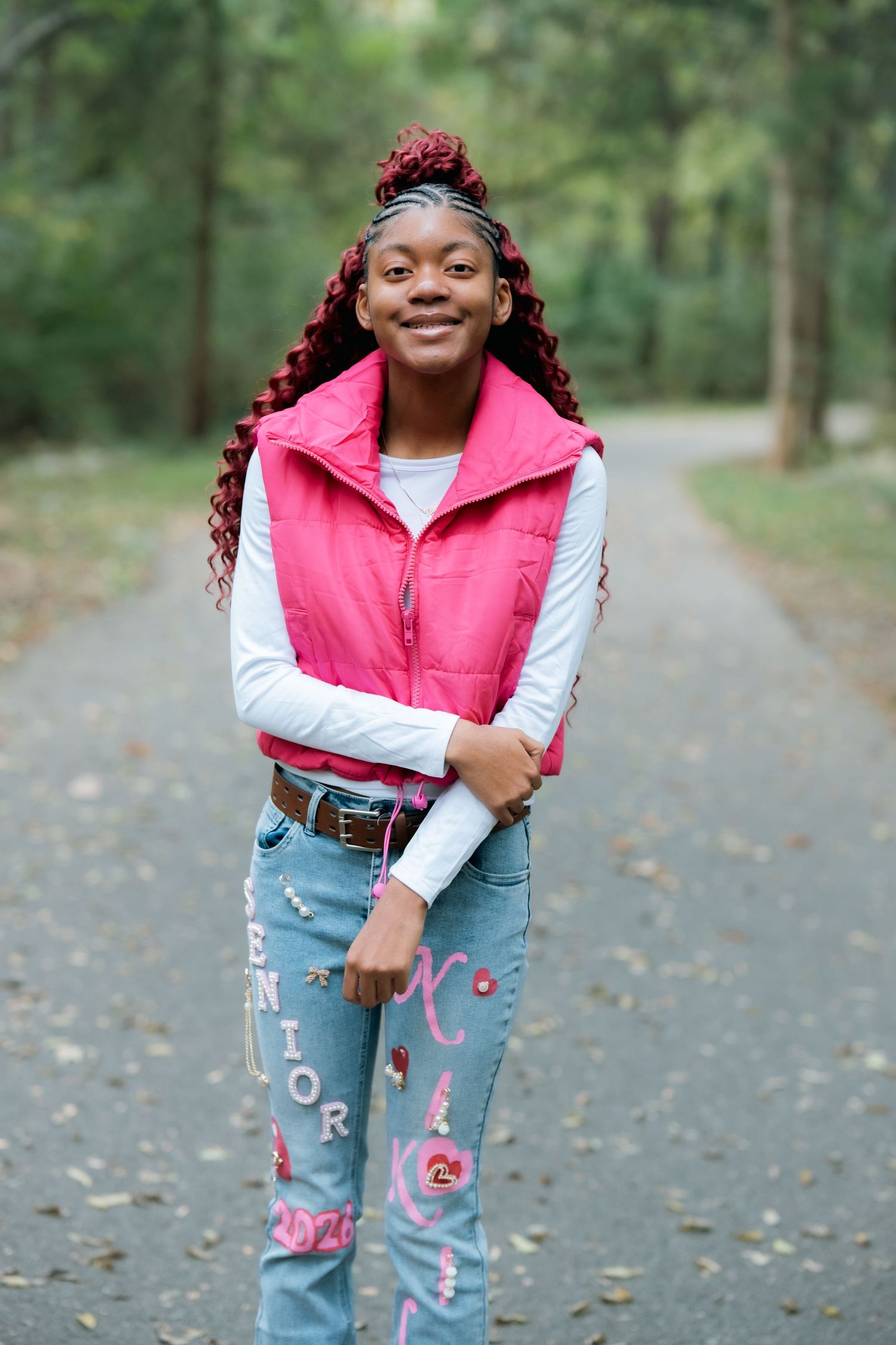 Pink vest and decorated jeans outfit photographed on a wooded path.