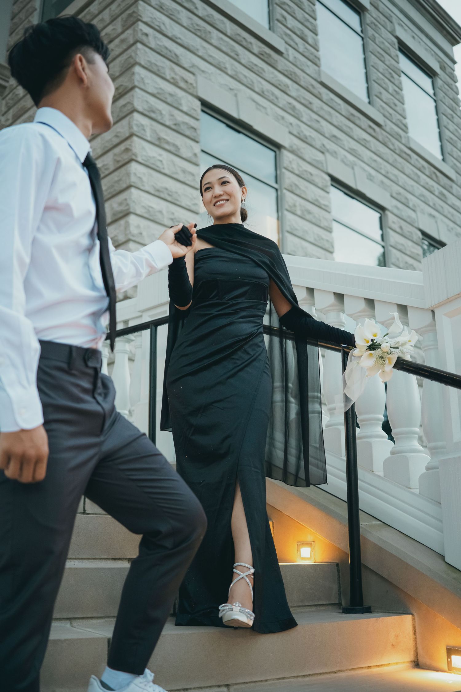 Two people in formal attire walk up an elegant staircase with illuminated steps.