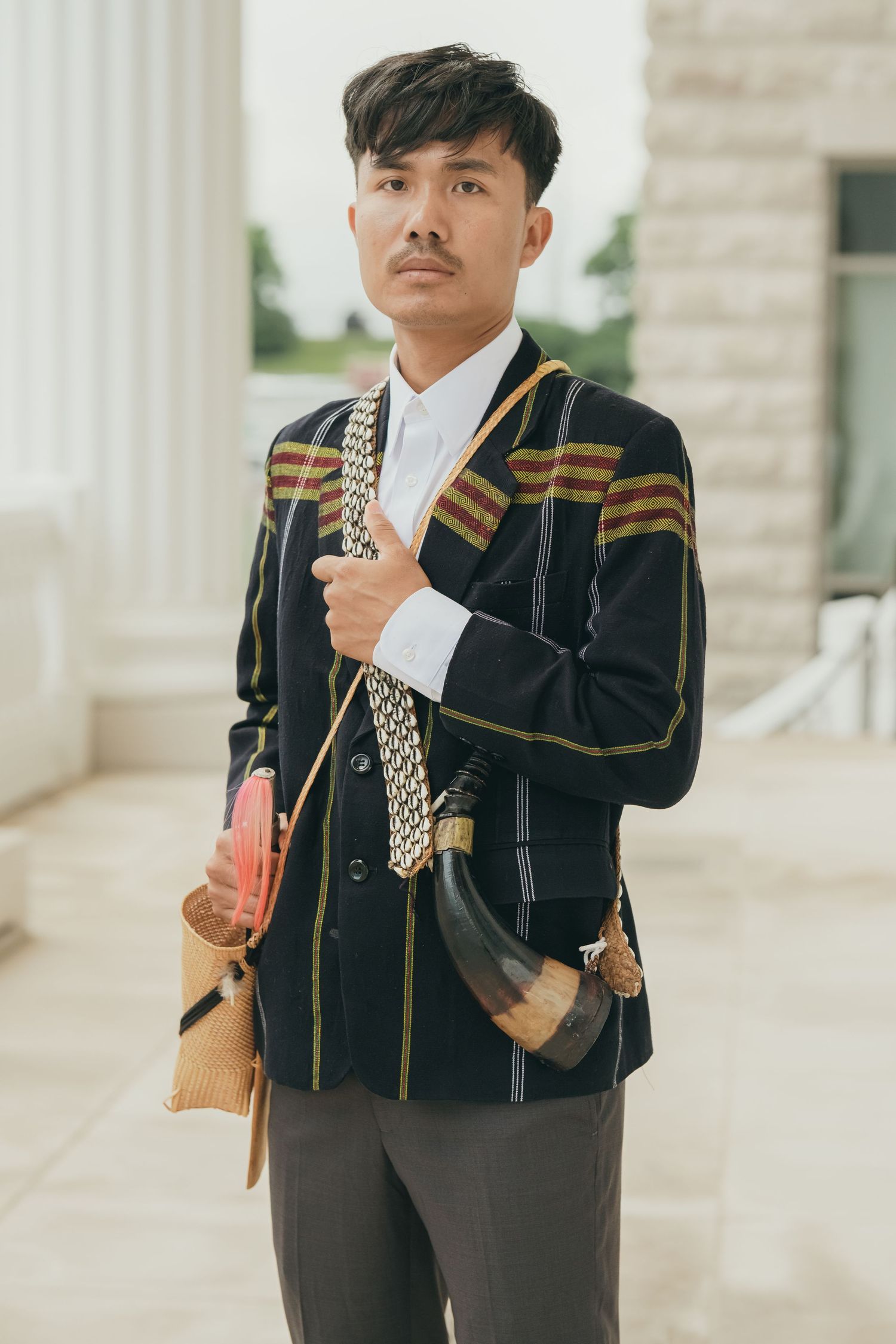 A person in formal attire with gold accents poses in front of white architectural columns.