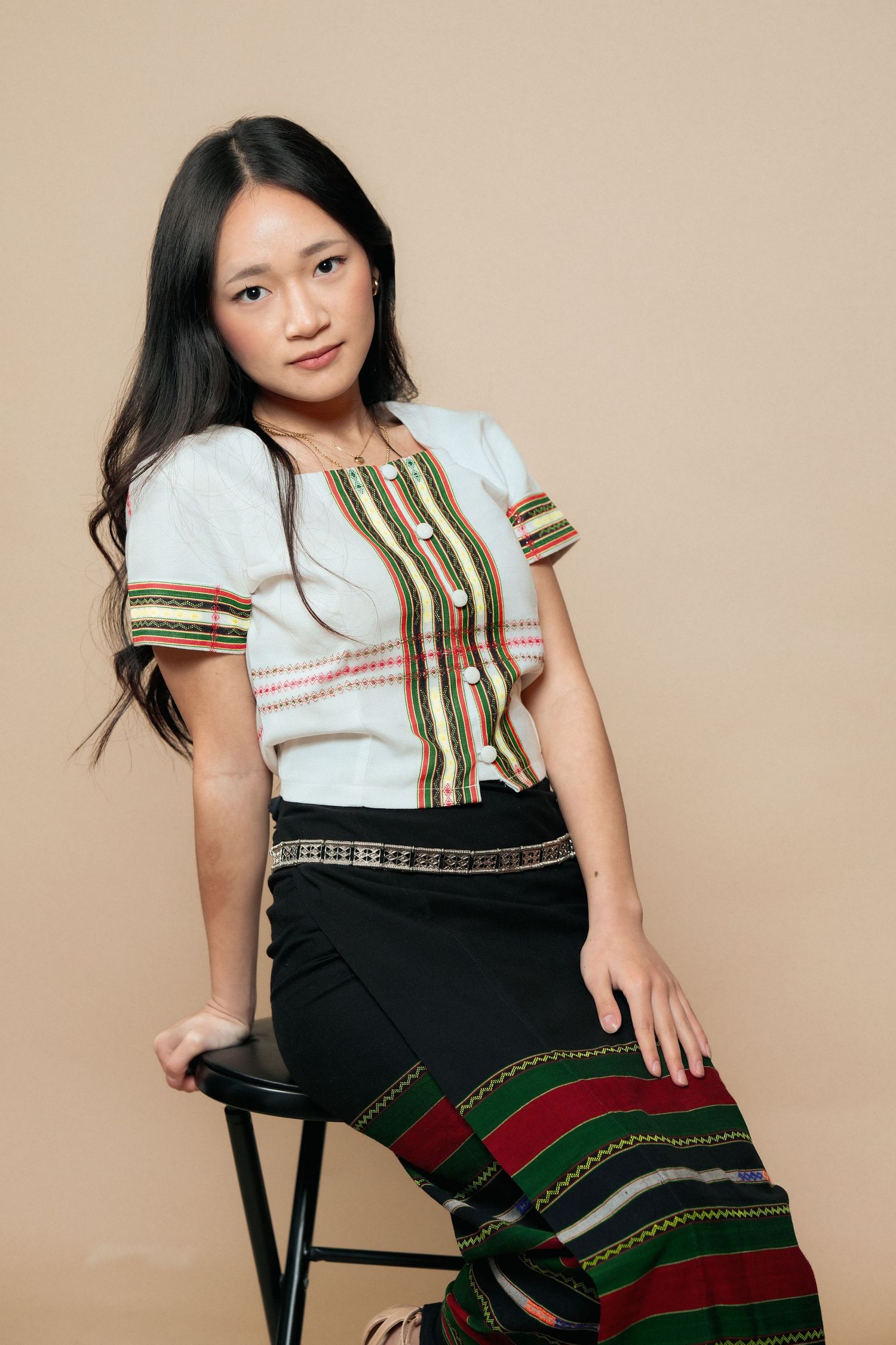 Model wearing white ethnic top with green stripes and black skirt with traditional embroidery.