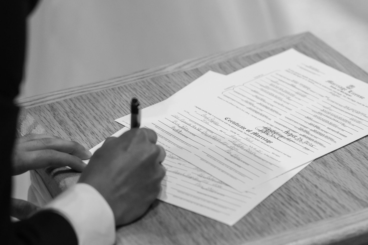 Close-up of hands signing marriage documents on wooden surface.