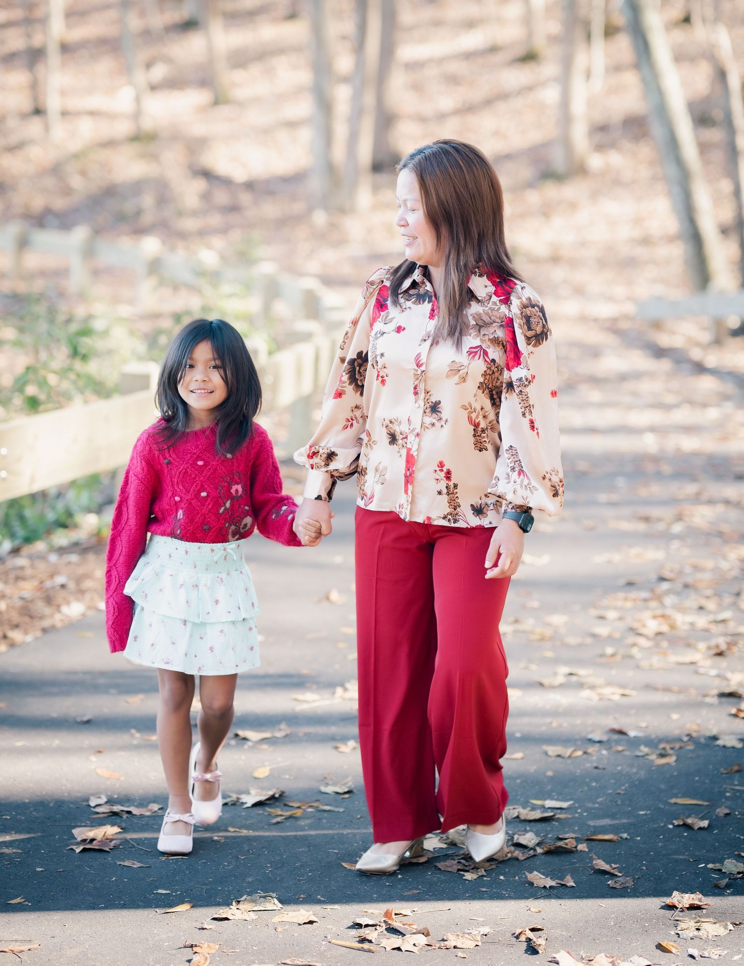 Two people in red and floral outfits play together on a leaf-covered path.