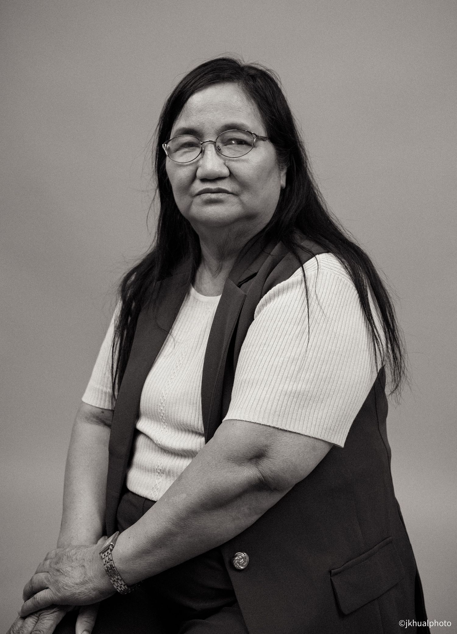 A person wearing glasses and a dark vest over white shirt poses against grey background.