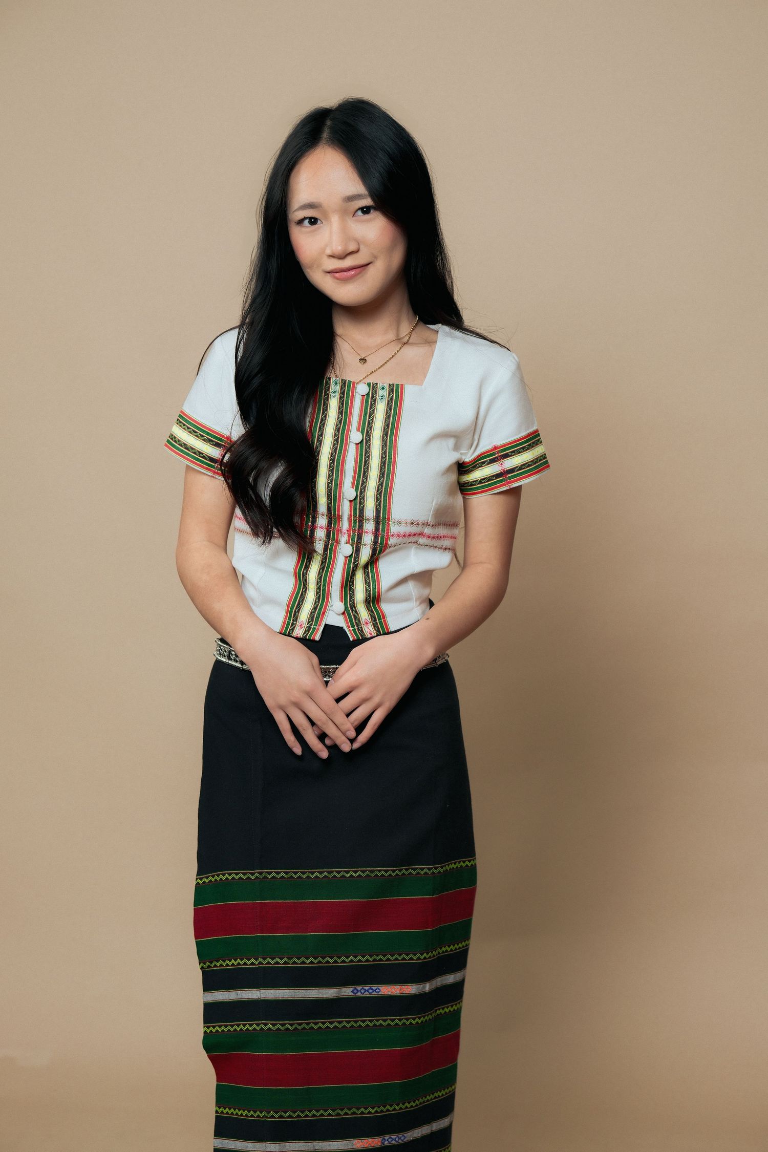 Person wearing white and green traditional top with striped skirt poses confidently.