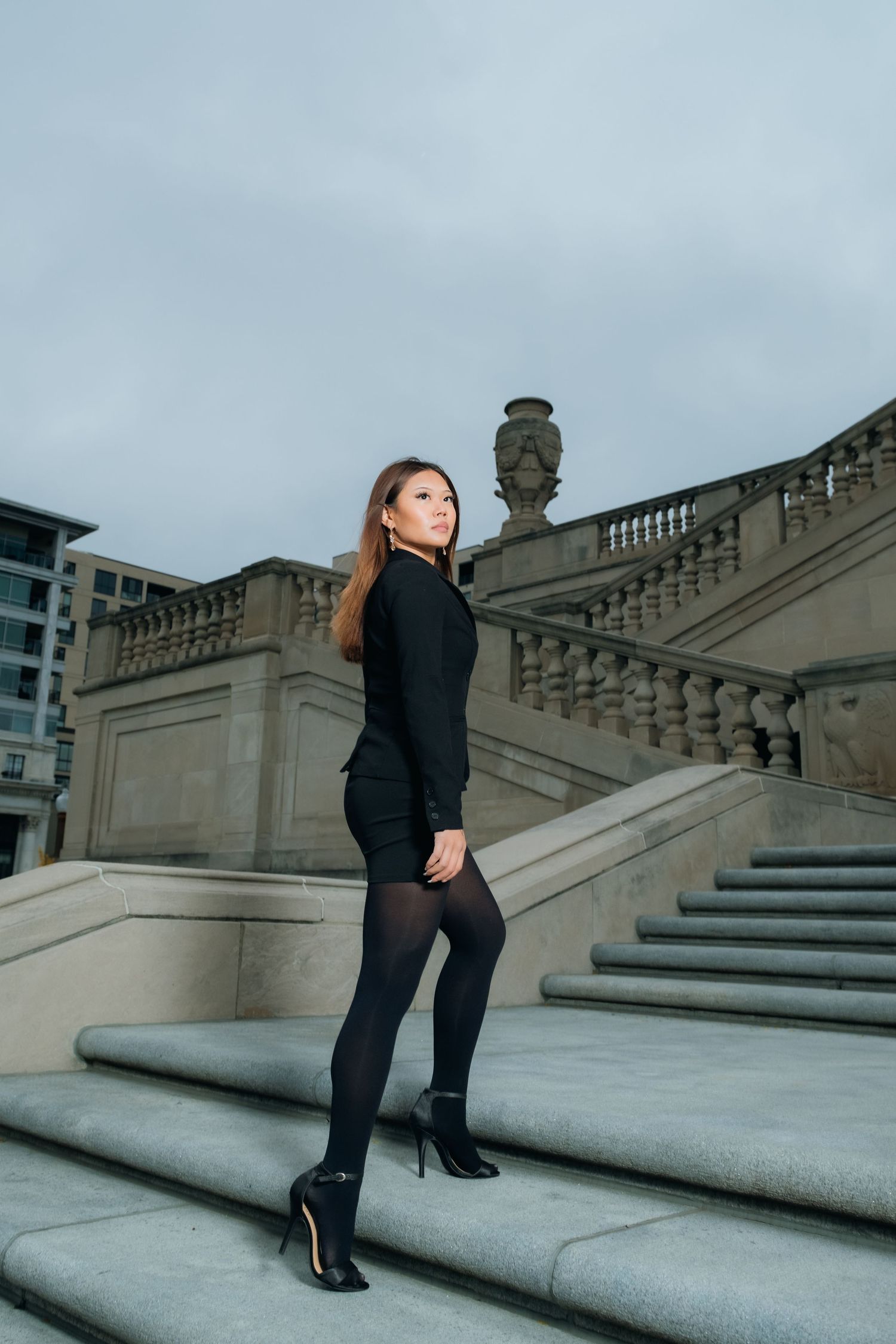 Fashion model in all black outfit poses on grand stone staircase with ornate architectural details.