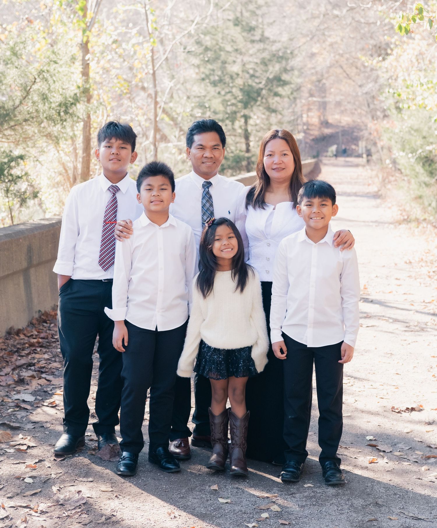 Family of six posing outdoors on a path surrounded by autumn trees, dressed in formal attire.