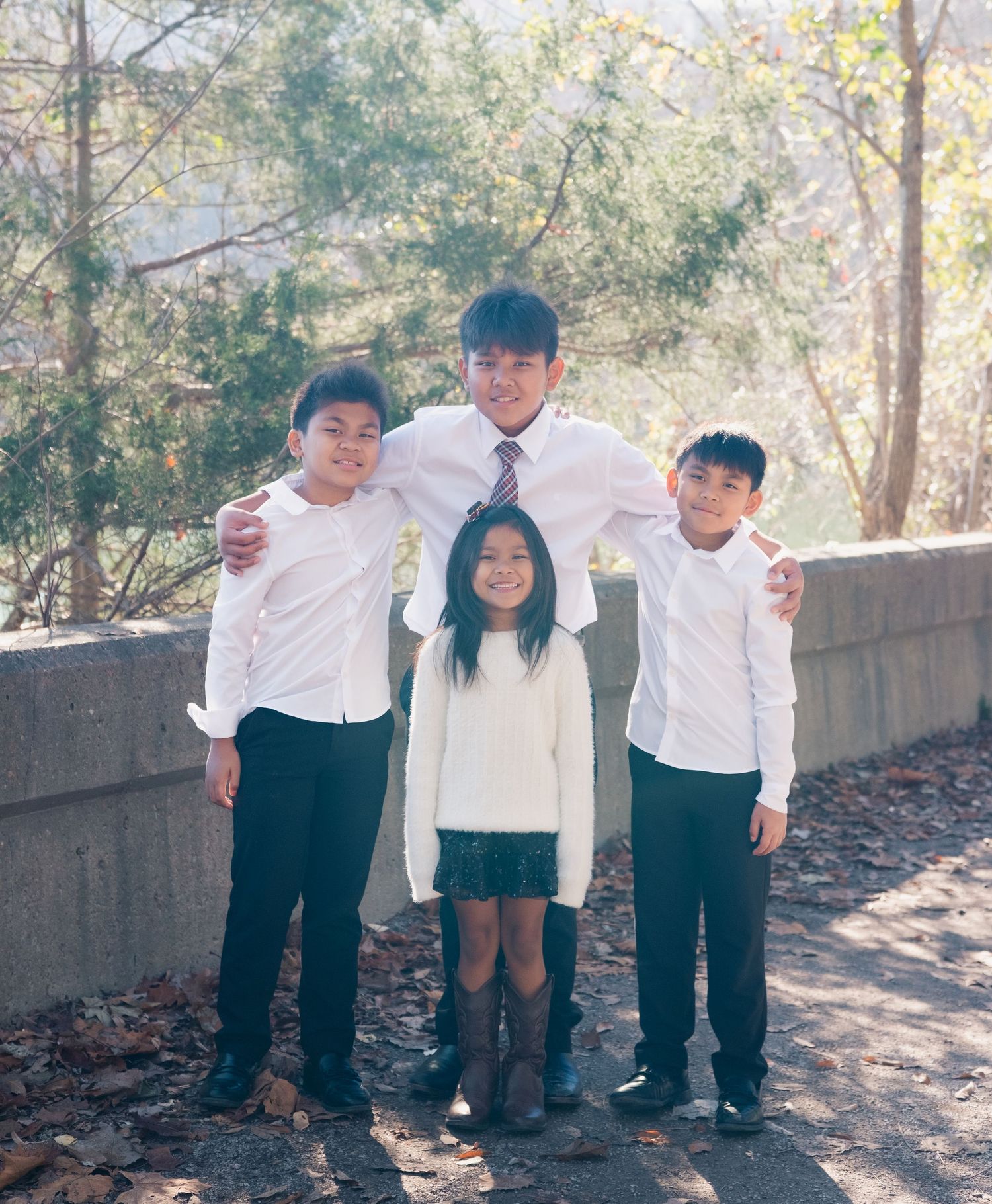 Children in matching white shirts and dark pants play and pose together on an outdoor path.