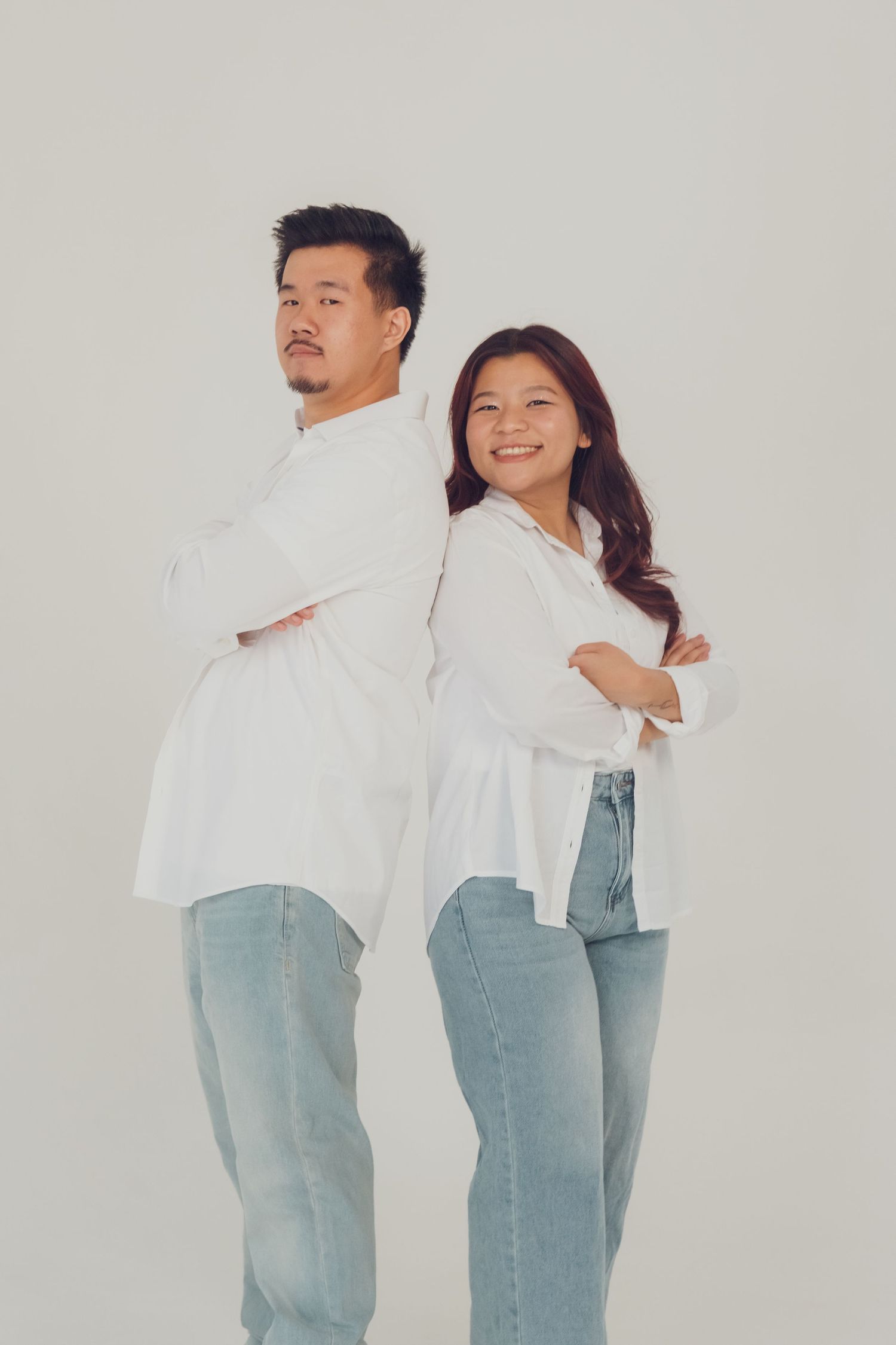 Two people in white shirts and jeans pose expressively against neutral backdrop.
