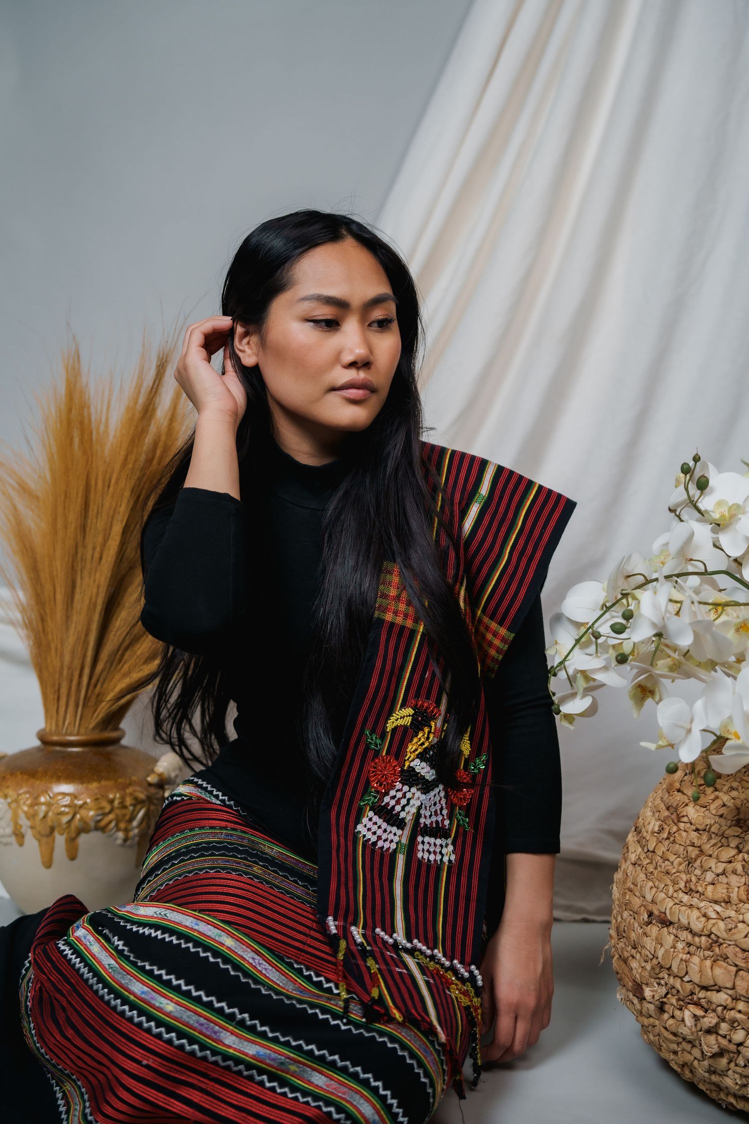 Artistic portrait with traditional woven garment against white backdrop with dried pampas grass.