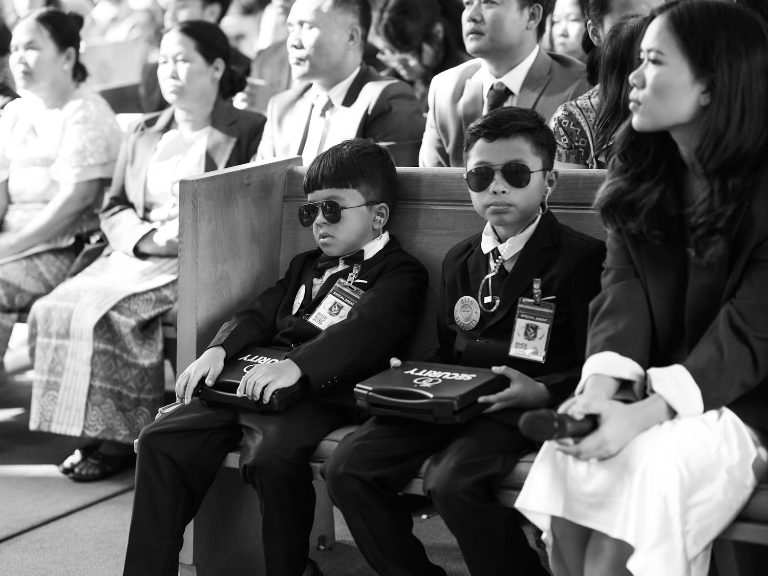 Two young boys in suits and sunglasses sit at a formal event in this black and white photo.
