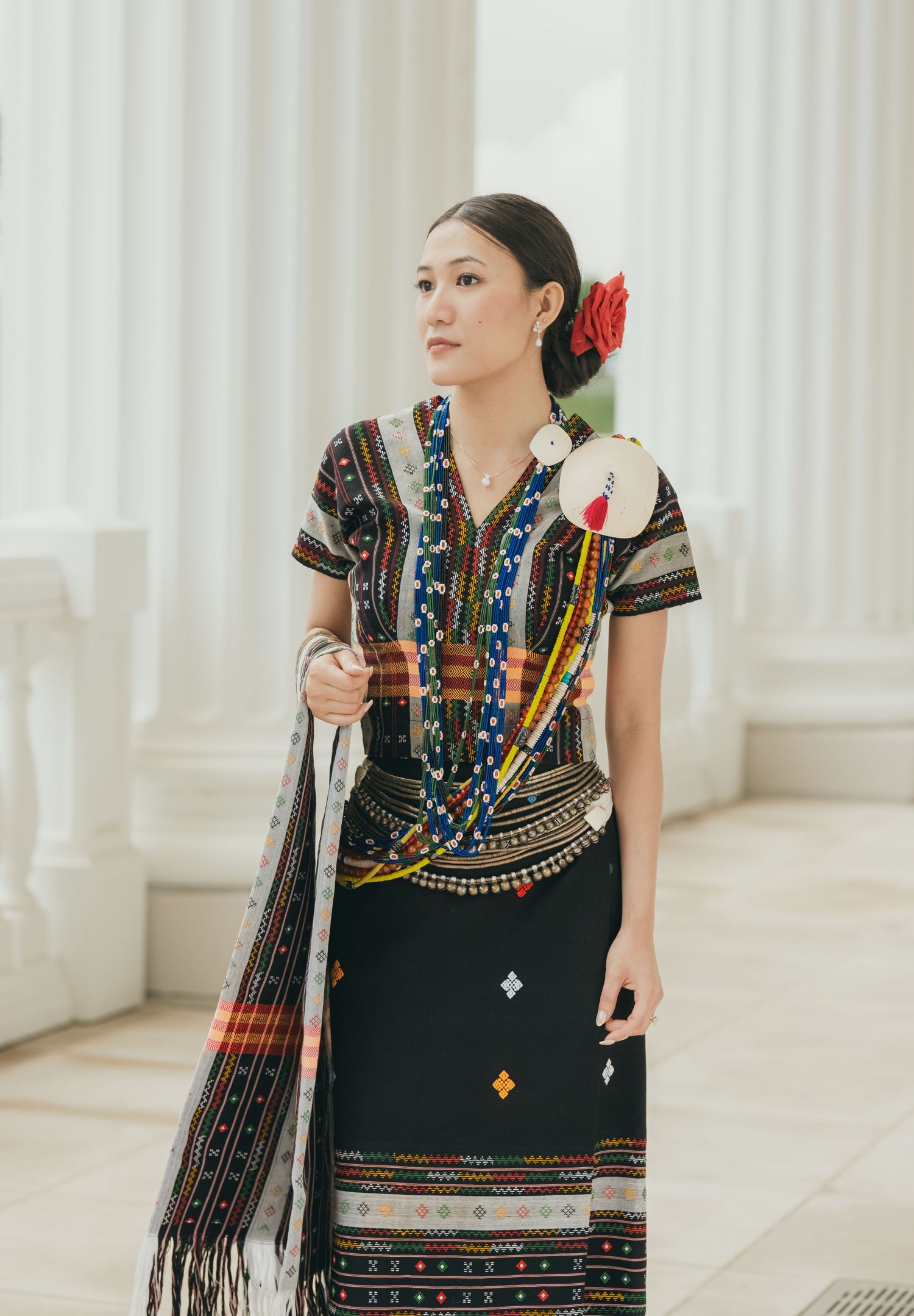 Traditional ethnic dress with colorful embroidery and beaded details displayed against white columns.