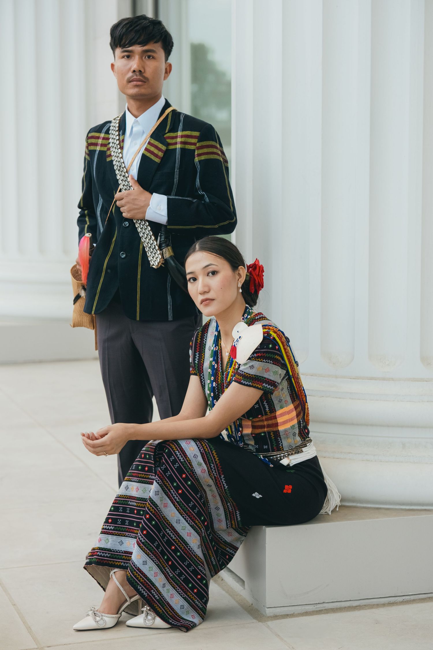 Traditional ethnic costumes photographed in an elegant white-columned architectural setting.
