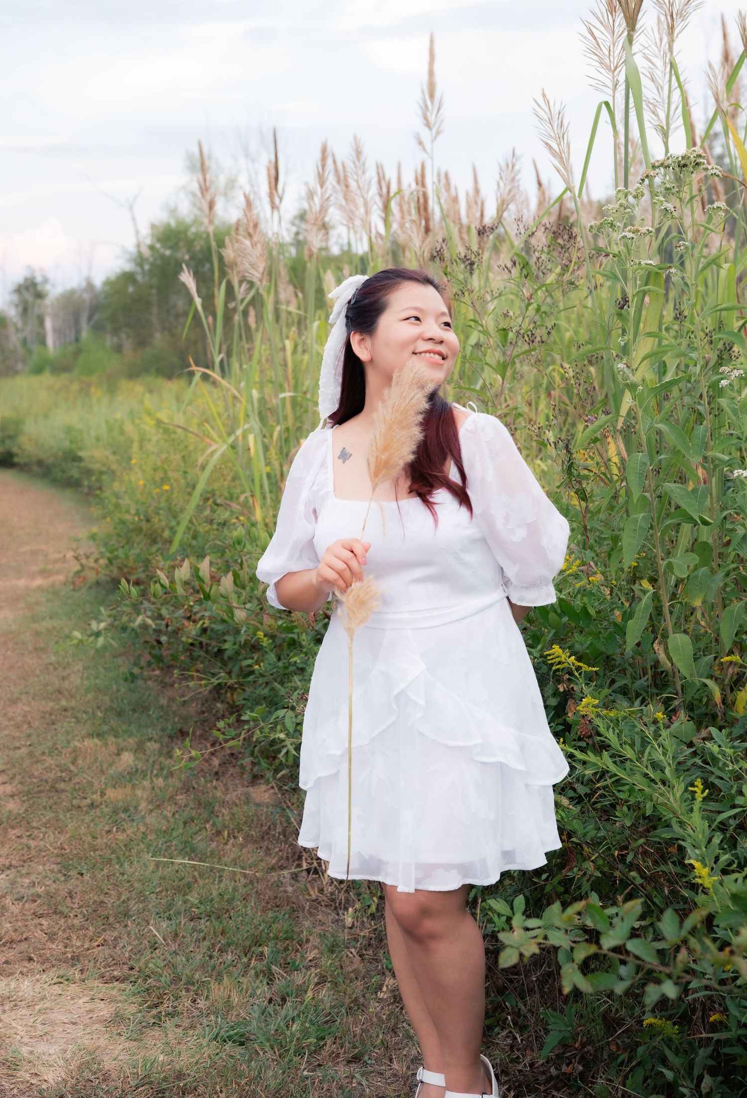 A figure in white dress twirls joyfully among wildflowers on a dirt path.