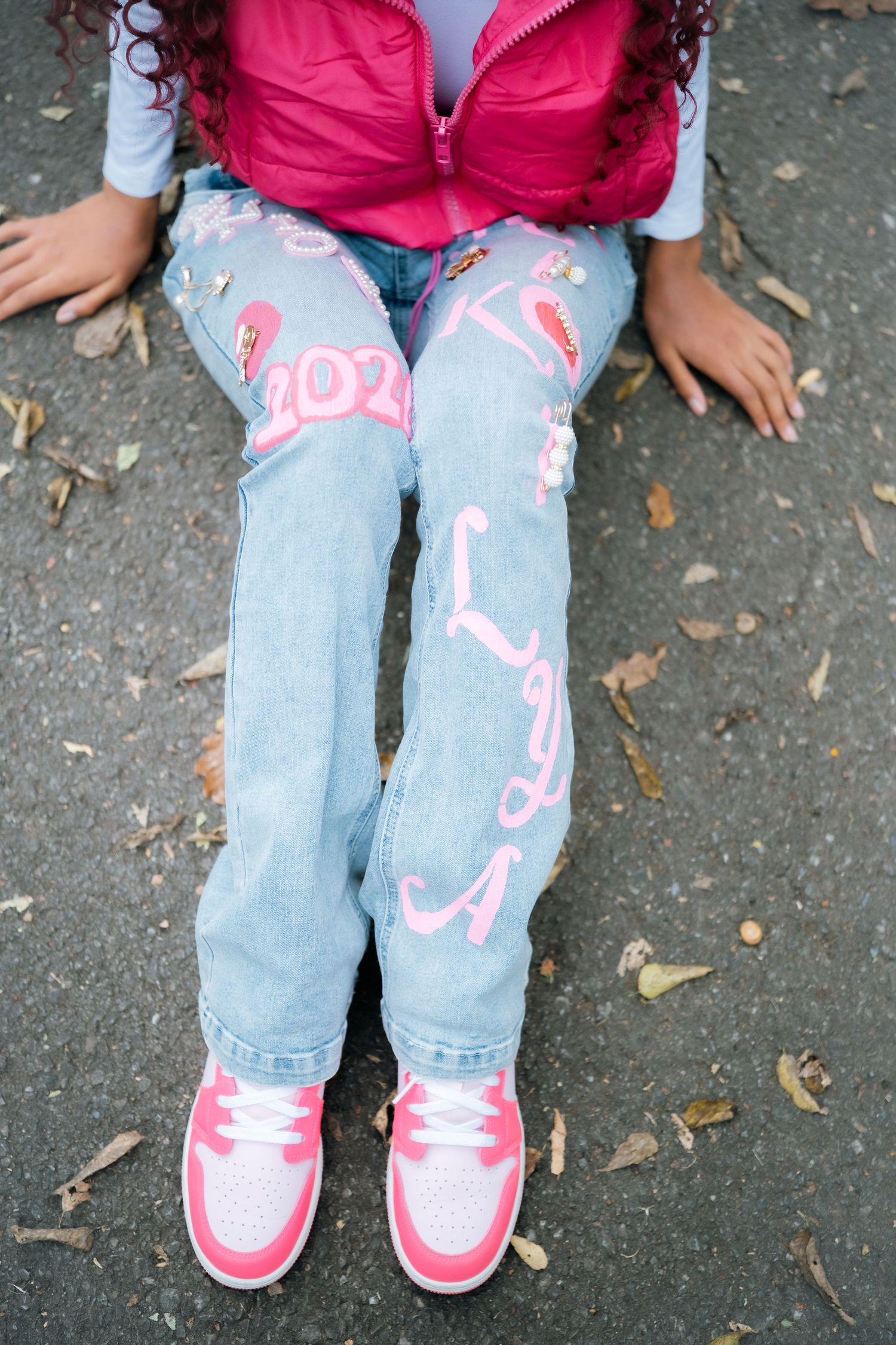 Close-up view of light blue jeans with pink decorative text and matching pink sneakers.