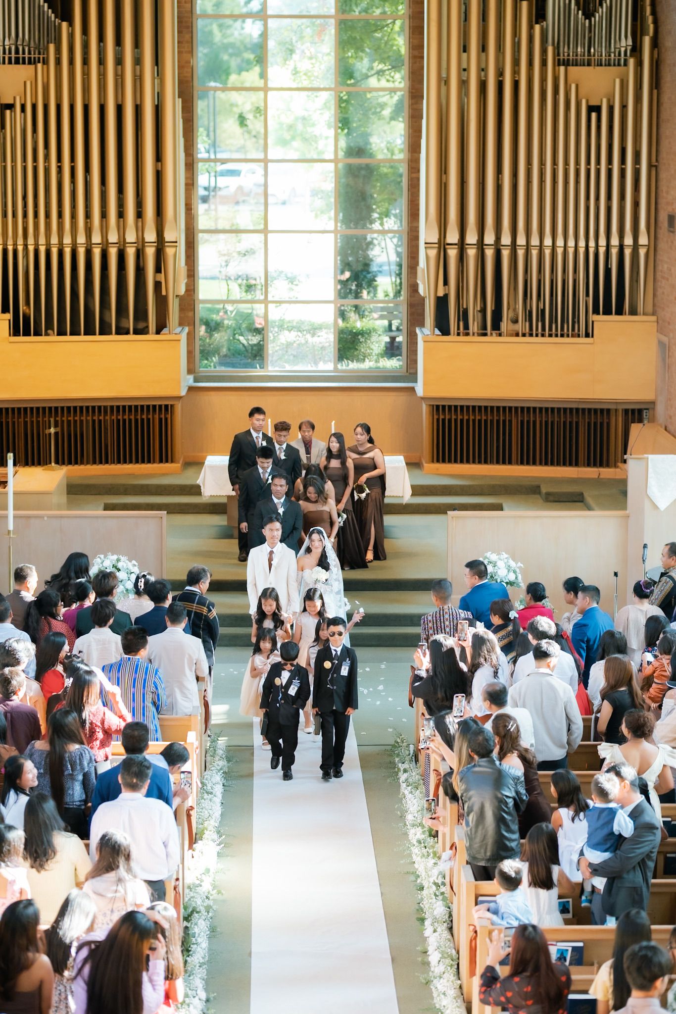 Guests fill church pews as wedding party walks down aisle beneath grand organ pipes.