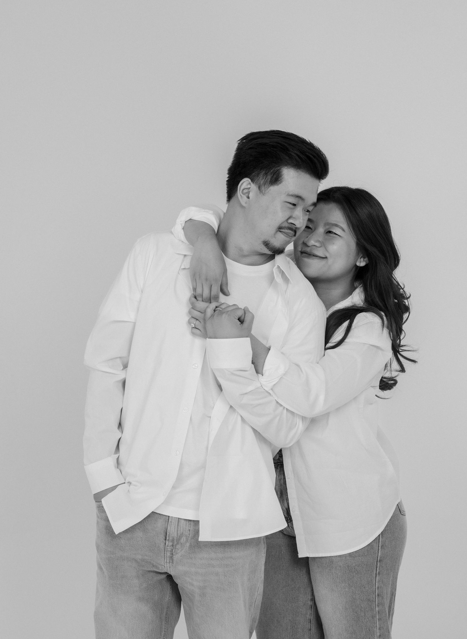 Couple in white shirts and jeans share intimate black and white portrait moment.