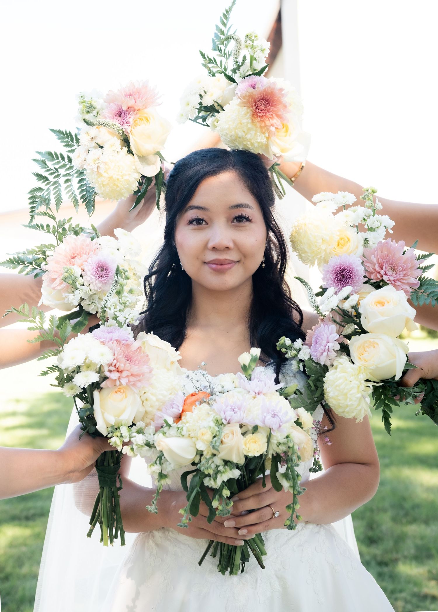 Bride with elegant bouquet of pink and white flowers framed by floral arrangements outdoors.