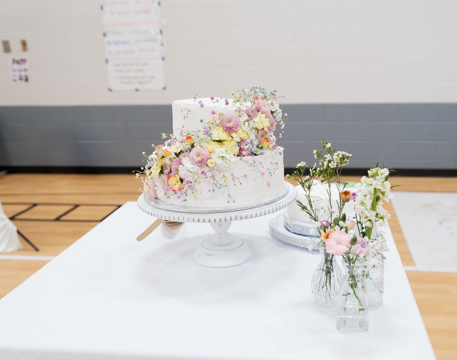 White wedding cake with floral decorations displayed on an elegant table setting.