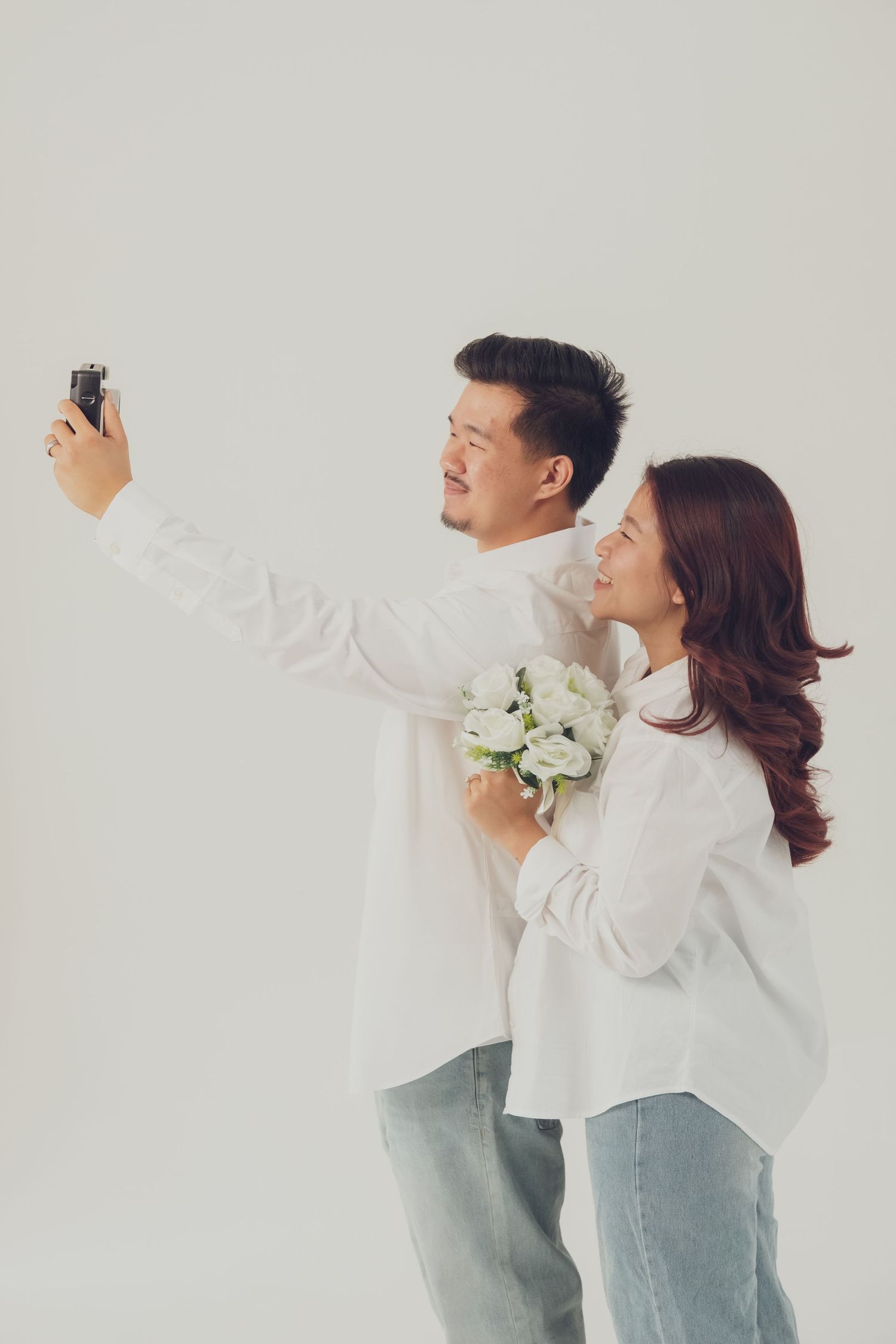 Couple in coordinated outfits poses energetically against white studio backdrop.