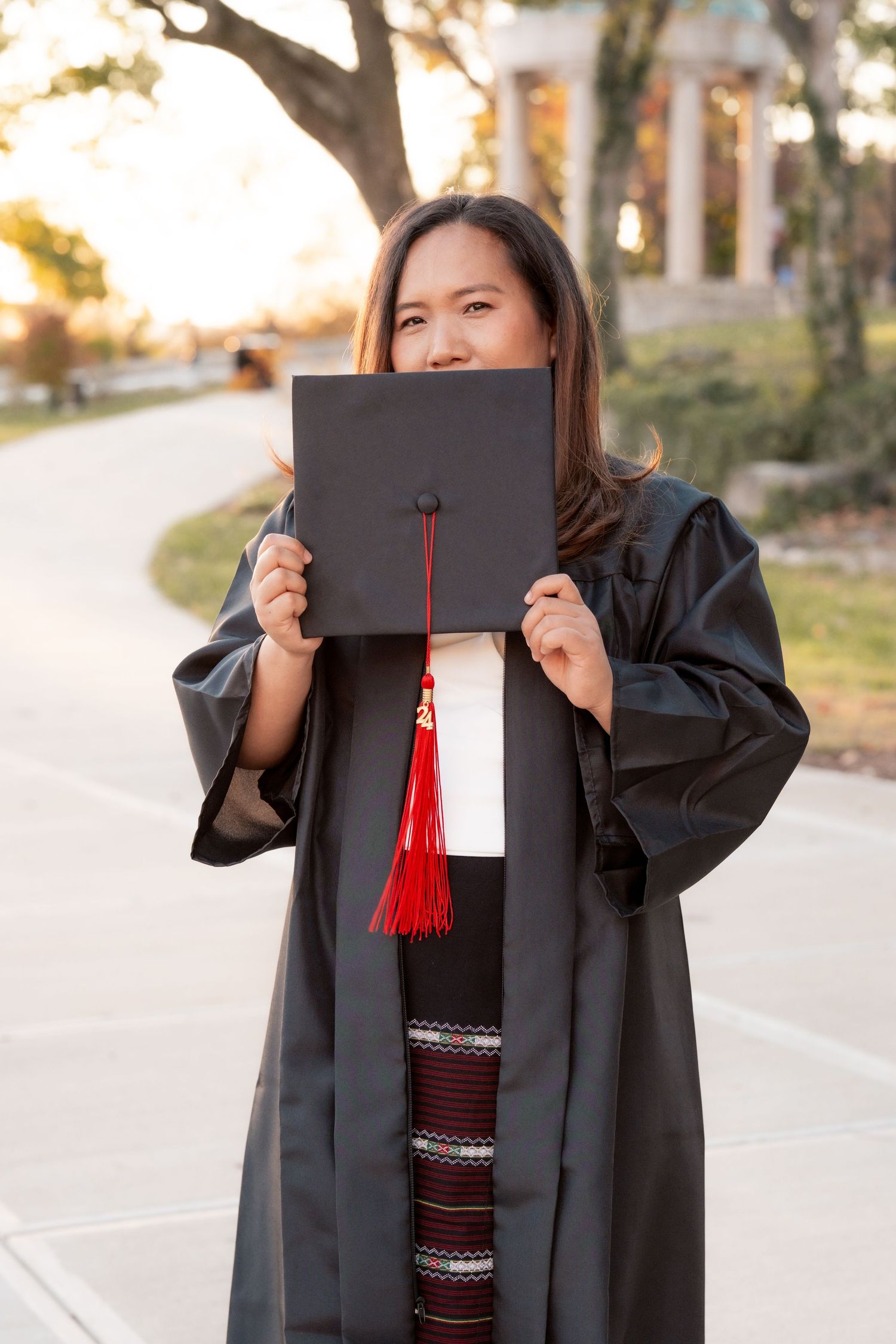 Graduate holds diploma holder while wearing traditional black graduation gown outdoors.