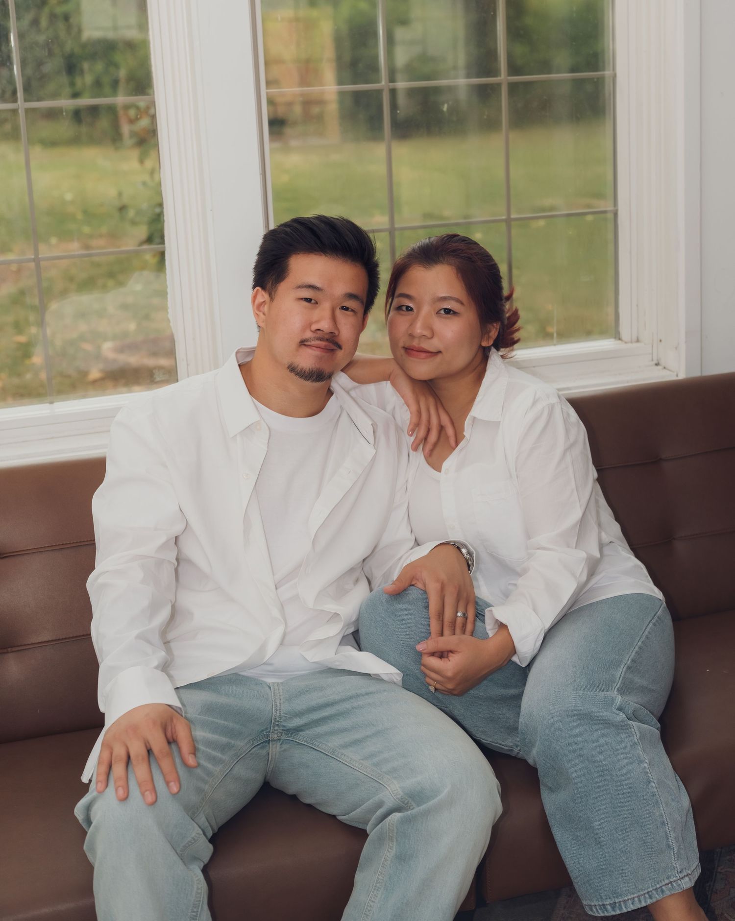 Couple in white shirts and light jeans shares intimate moment on brown leather sofa.