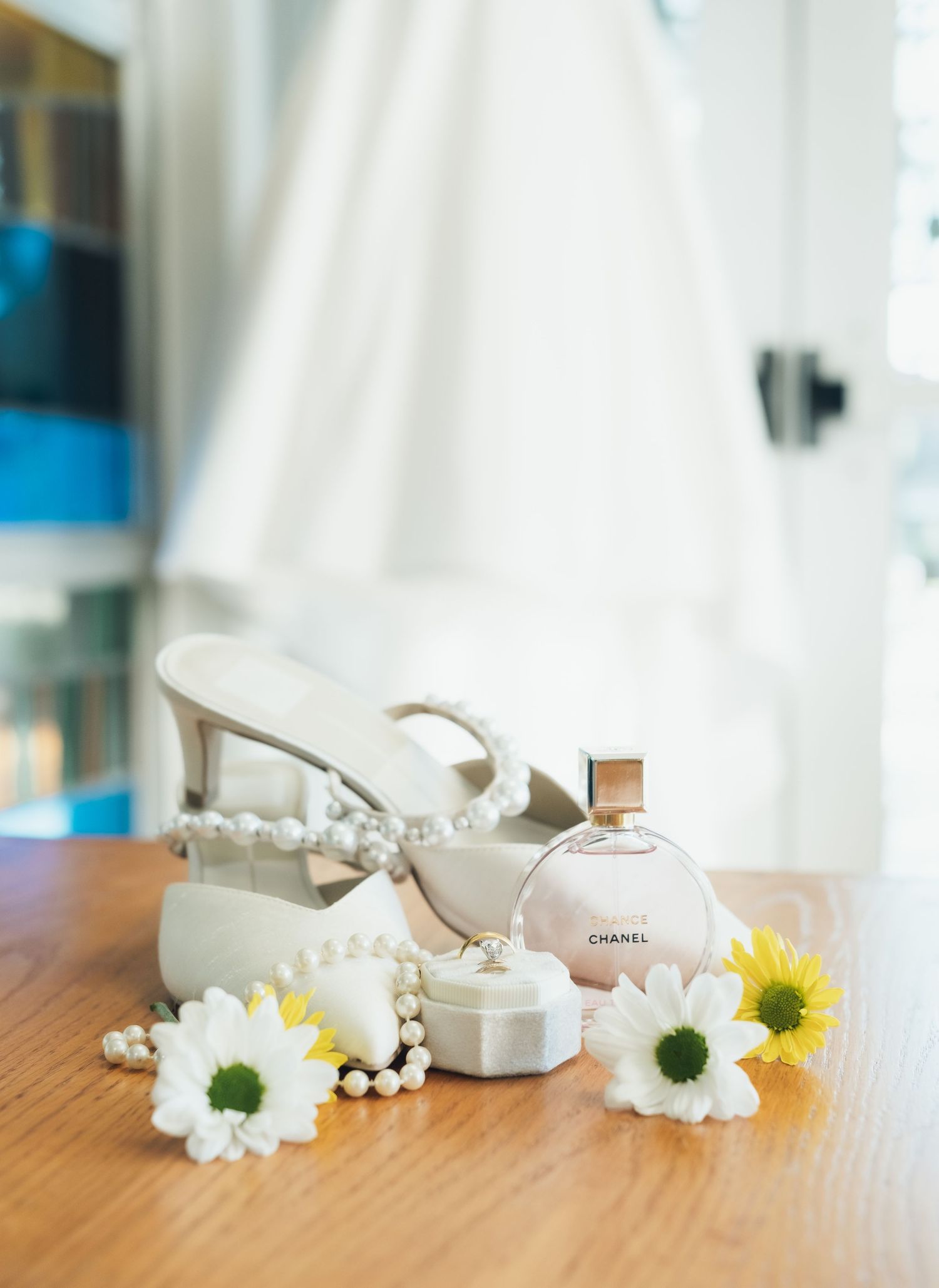 Elegant white bridal shoes and delicate daisies arranged on a wooden surface.