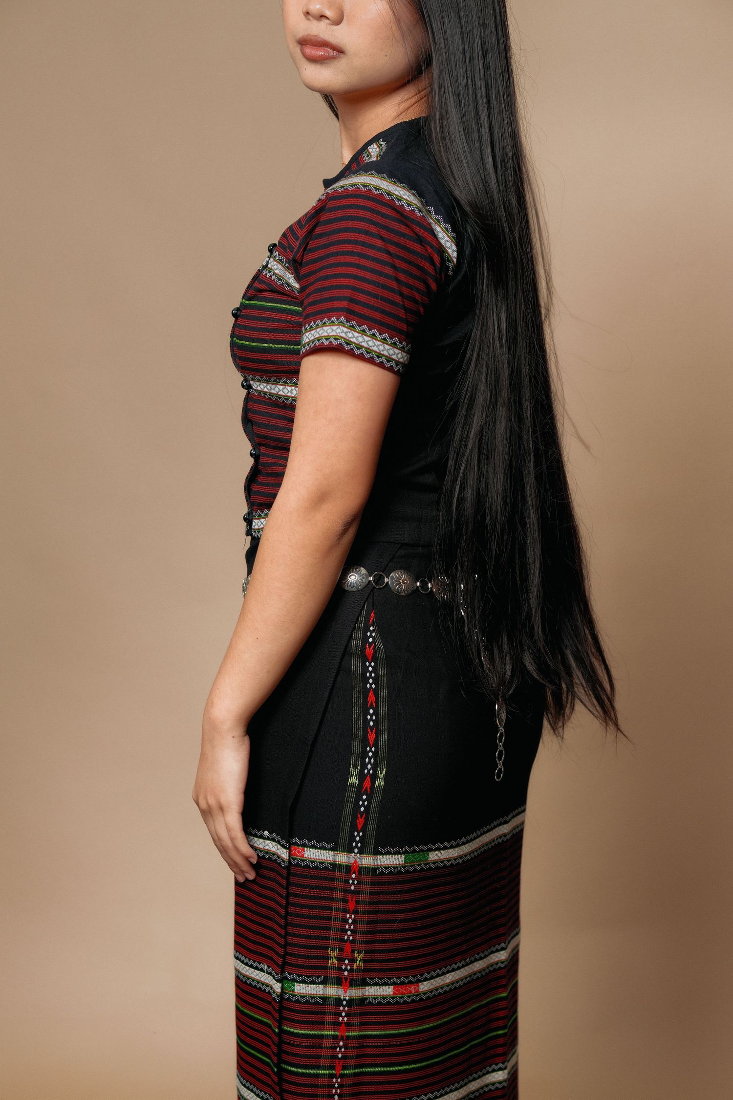 Side view of model in burgundy ethnic top with silver belt and black skirt.