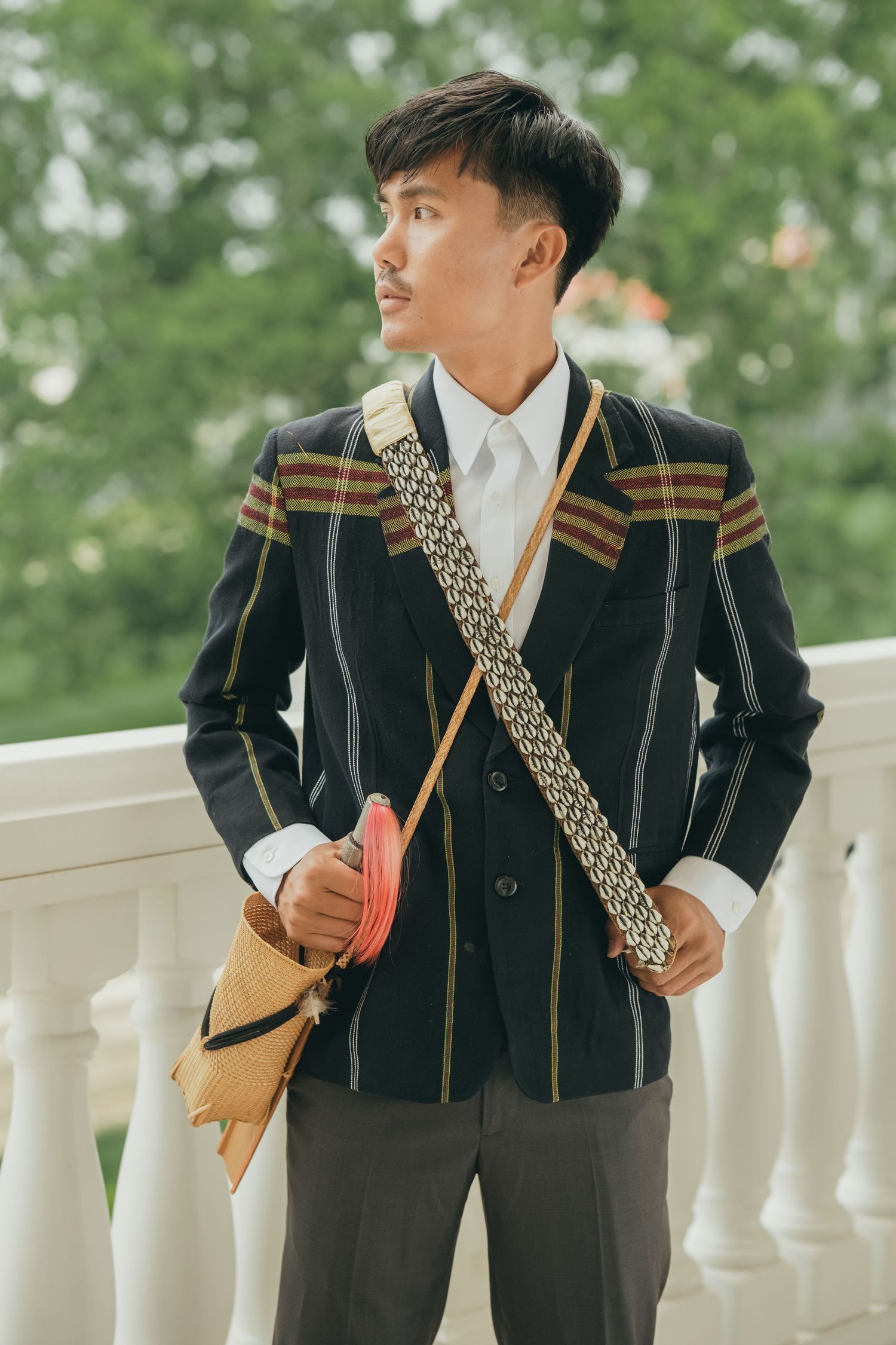 A person wearing a traditional black and gold striped formal outfit poses against white columns outdoors.