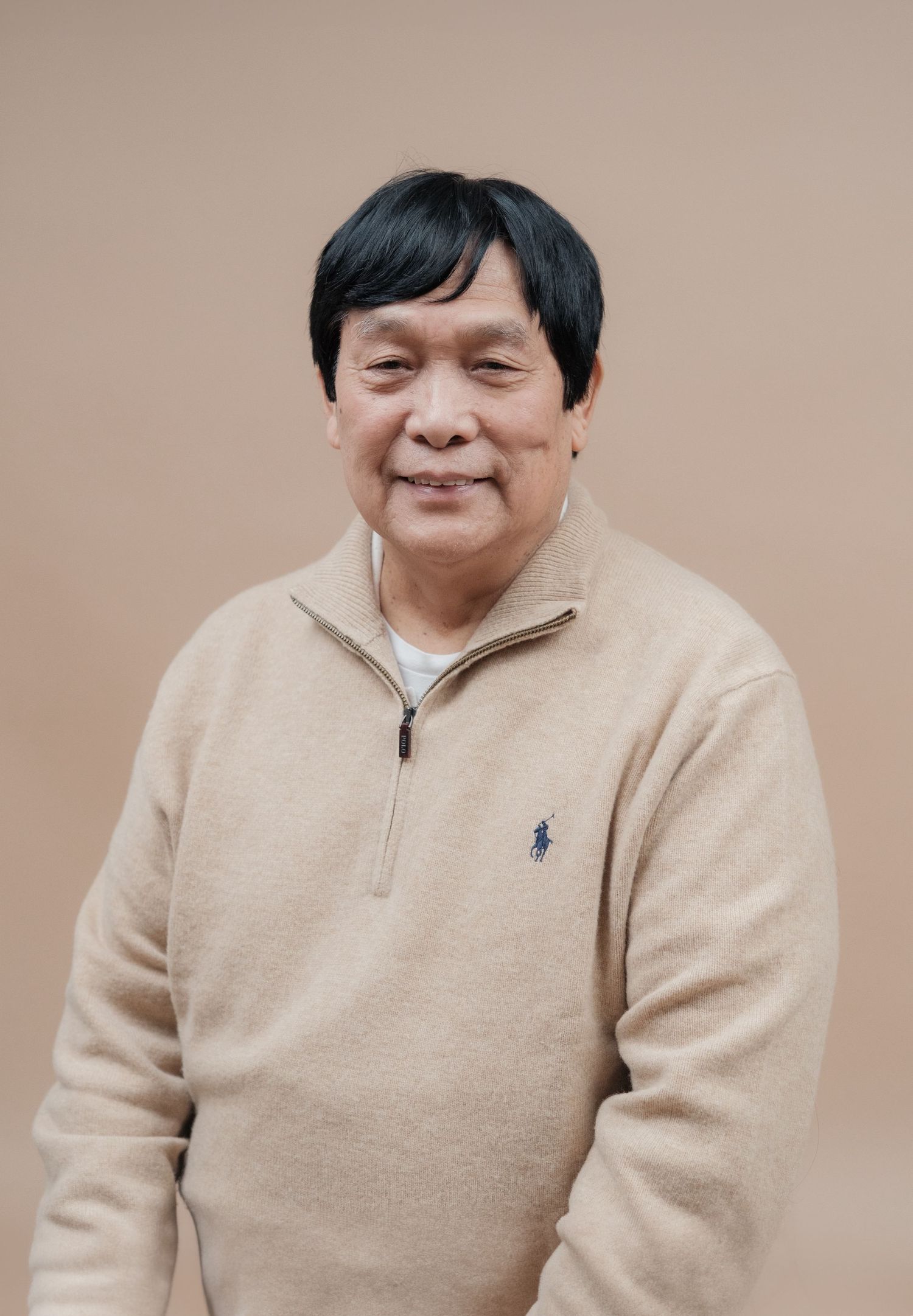 A person in a beige quarter-zip sweater smiling at the camera against a brown background.