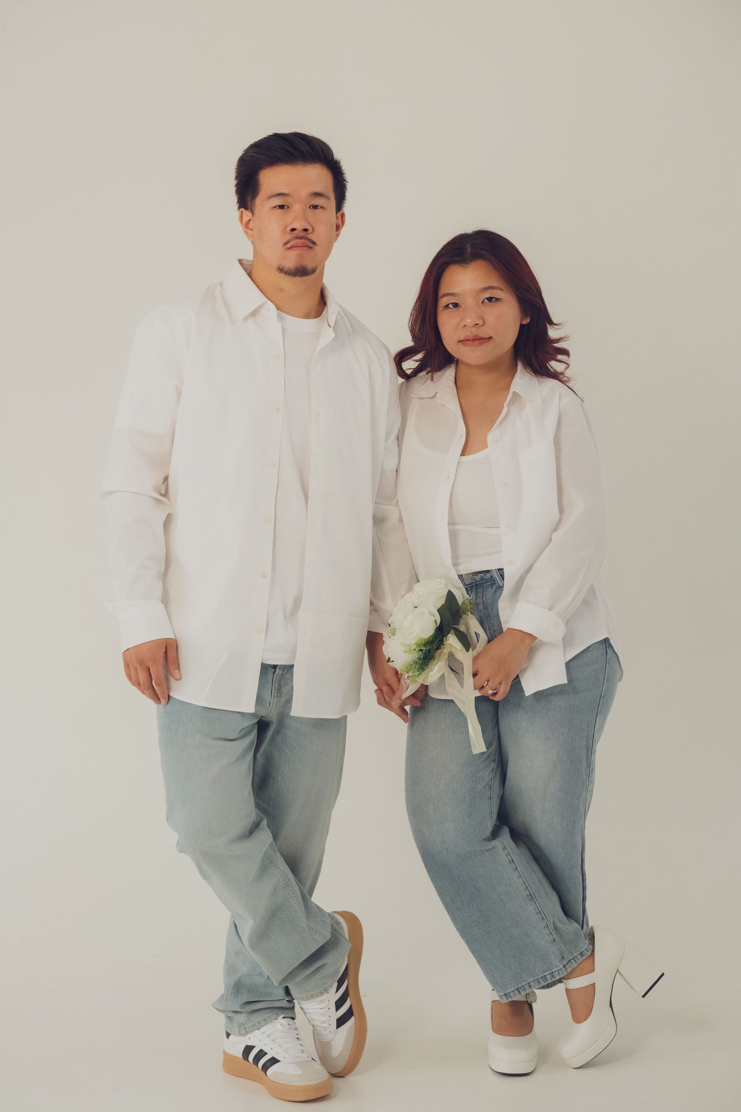 Casual studio portrait of couple in coordinated white shirts and light wash jeans.