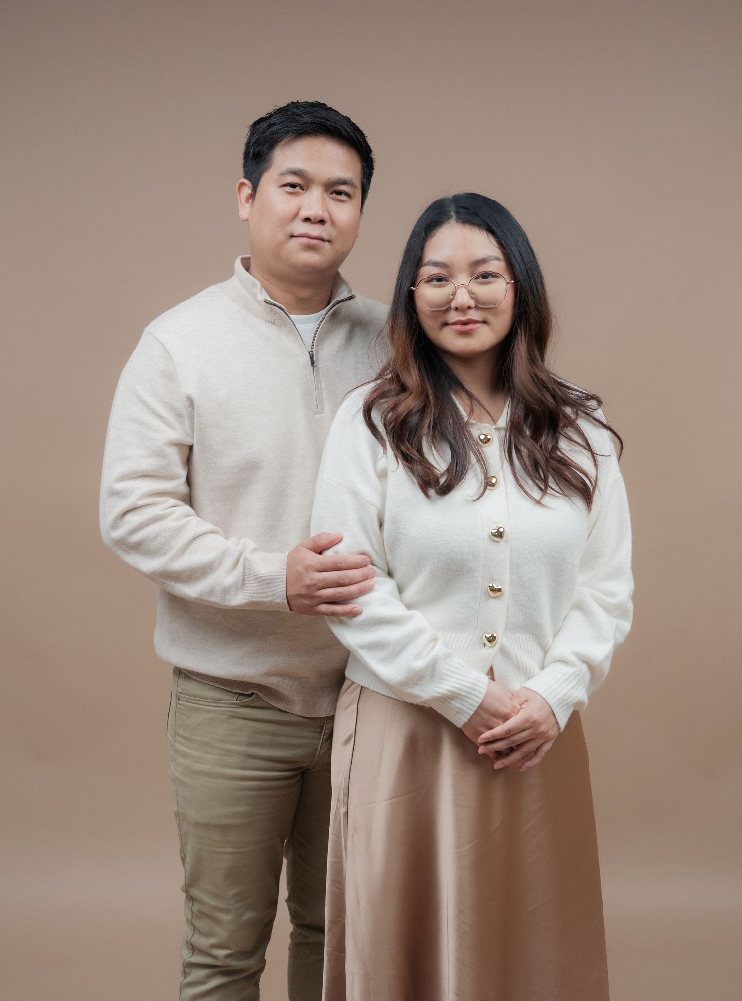 Minimalist family portrait series against beige backdrop wearing coordinated neutral outfits.