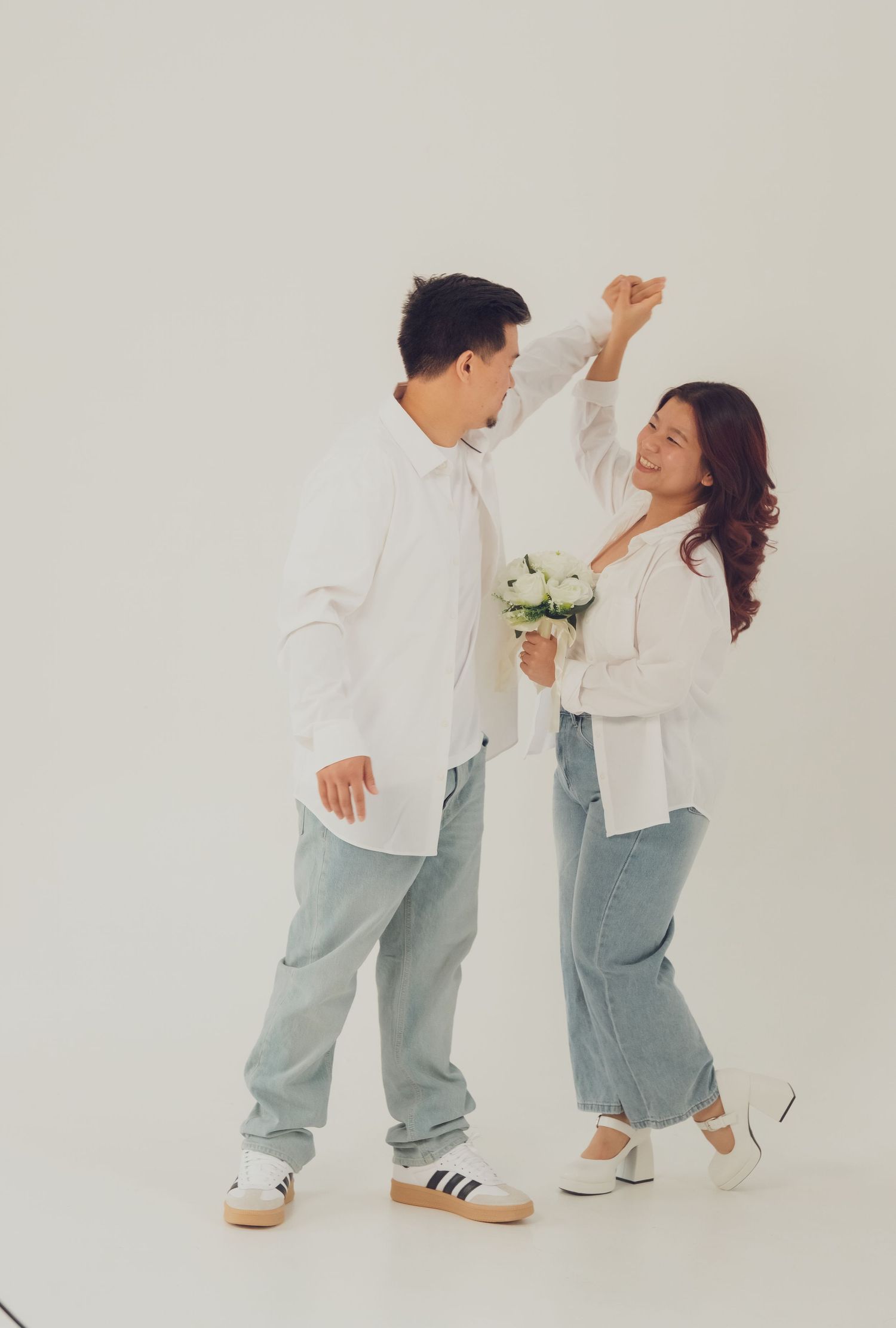 Couple in white button-downs and light denim creates dynamic poses in studio setting.