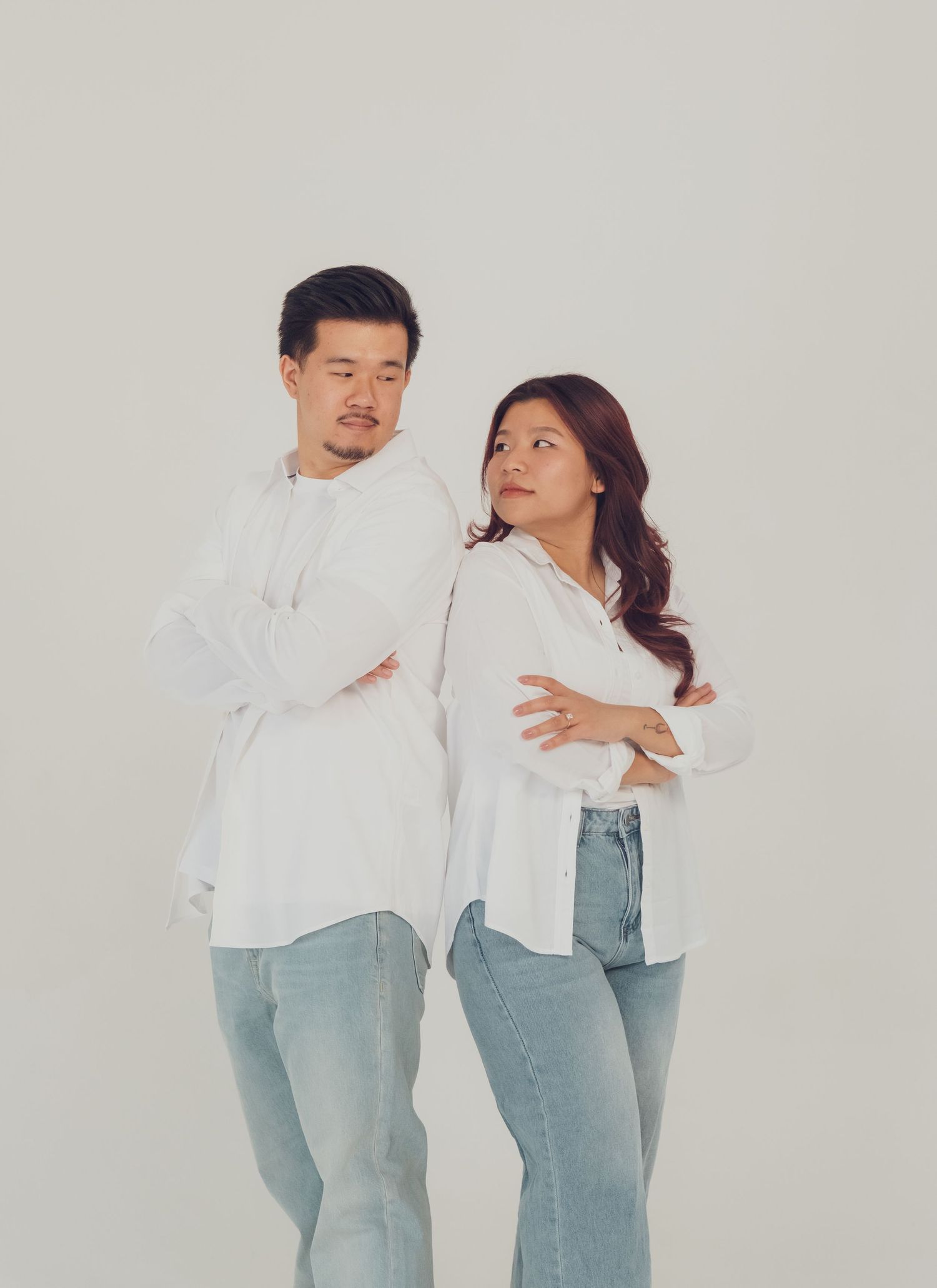 Two people in coordinated white shirts and jeans pose playfully against a neutral backdrop.