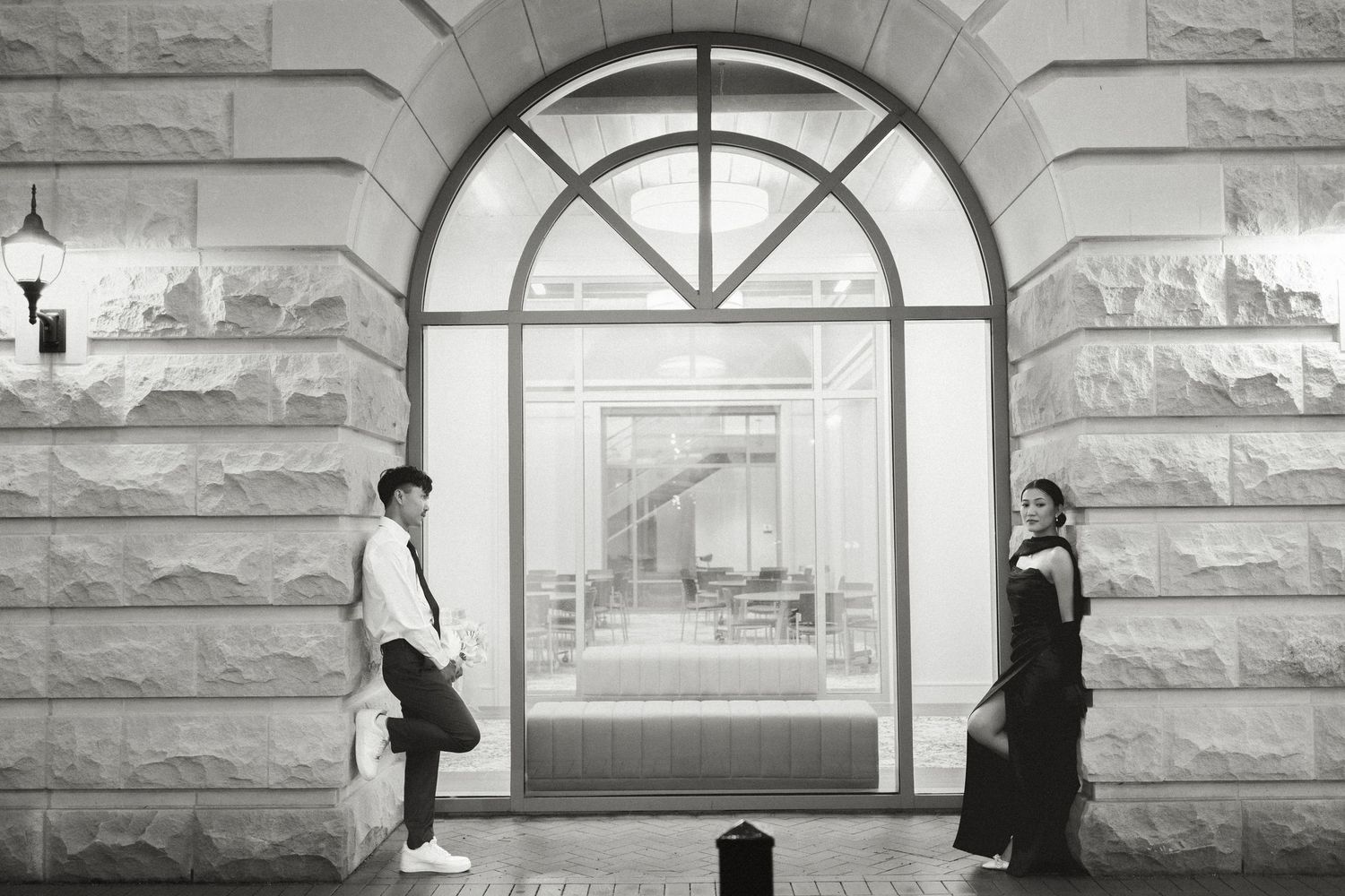 Silhouettes of people walking past large arched windows in a stone building.