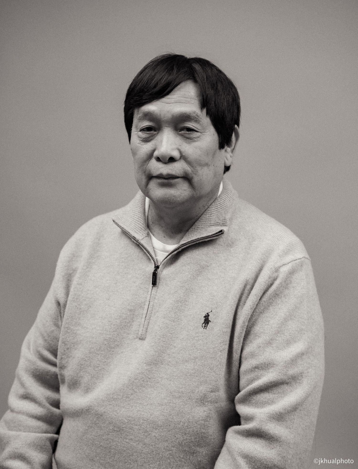 A person in a beige sweater poses against grey background for a portrait.