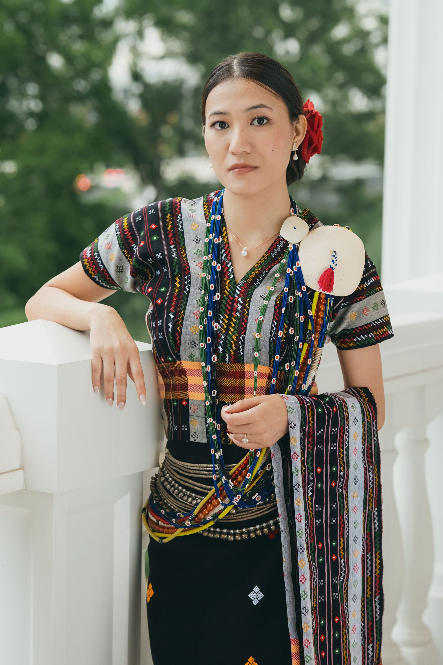 Traditional costume with intricate beadwork and red floral accent shown against white columns.