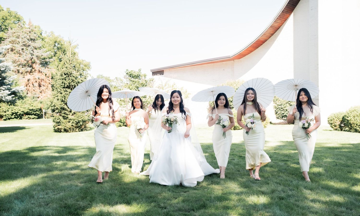 Wedding party in white dresses posing together on sunny outdoor lawn.