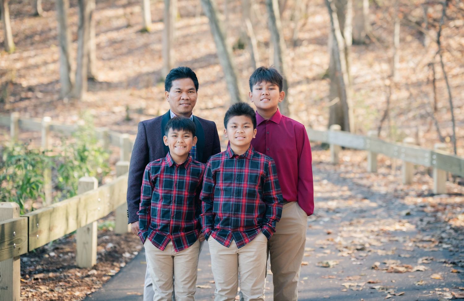 Family members in matching burgundy and plaid clothing stand together on an autumn forest trail.