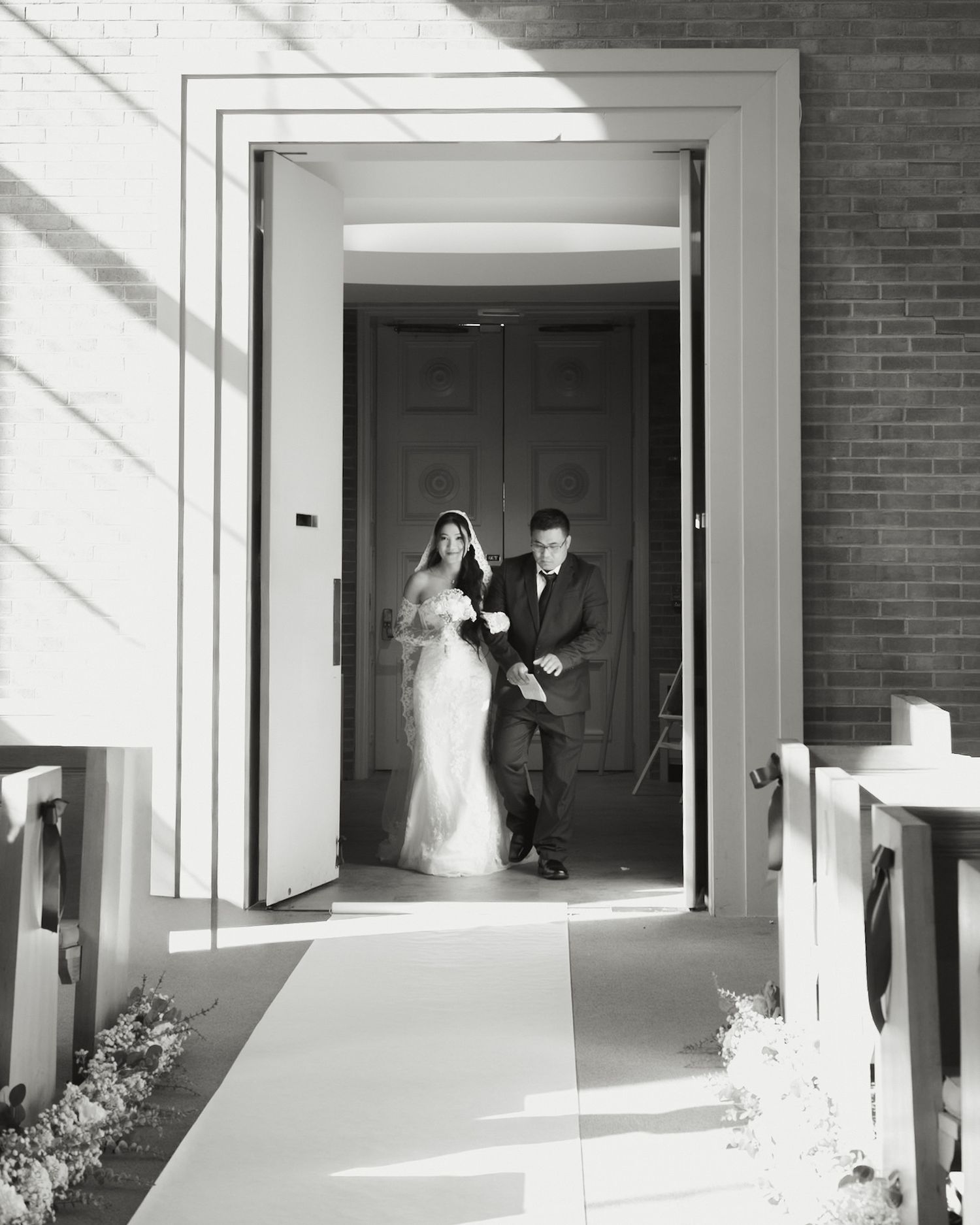 Bride and groom exit church through grand doorway in elegant black and white wedding photo.