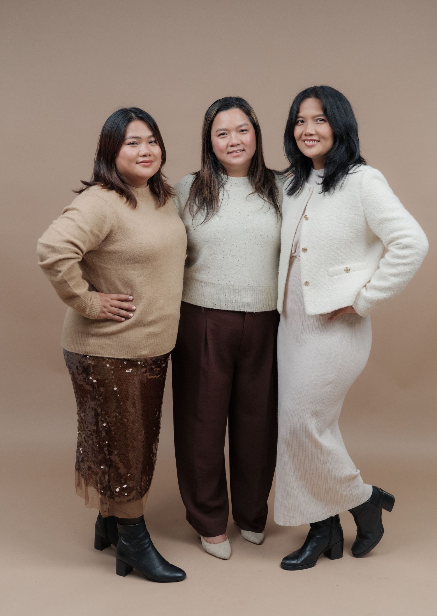 Three people in winter outfits featuring neutral tones and boots pose for a full-length portrait.