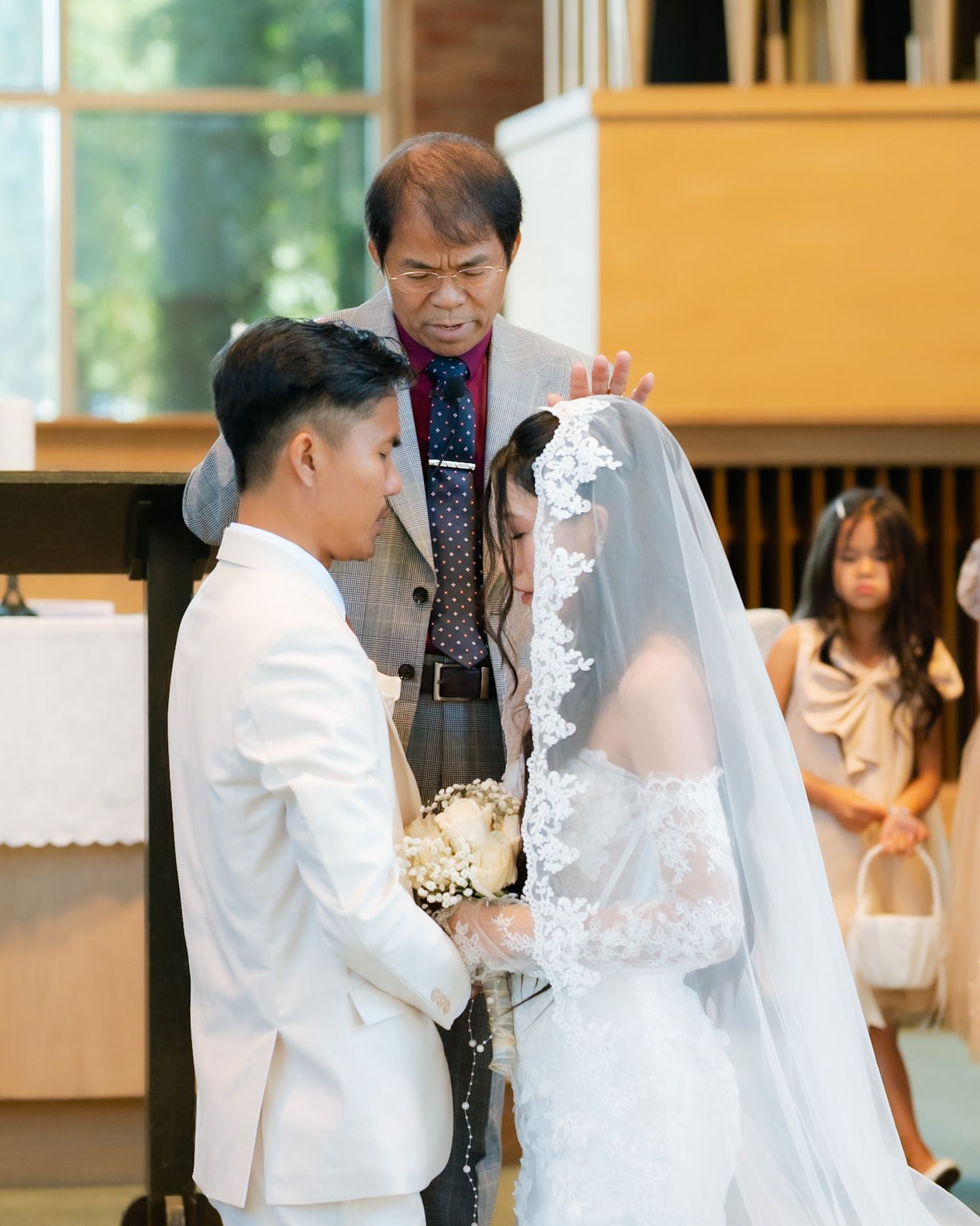 Officiant lifts bride's veil during intimate church wedding ceremony while groom holds her hands.