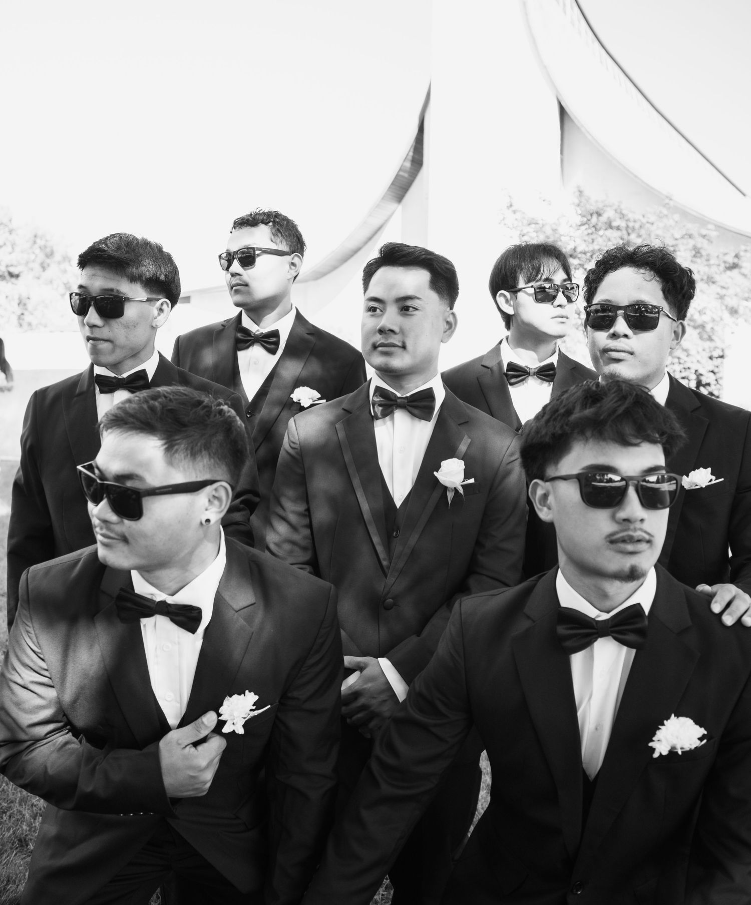 Groomsmen wearing sunglasses and black tuxedos pose together.