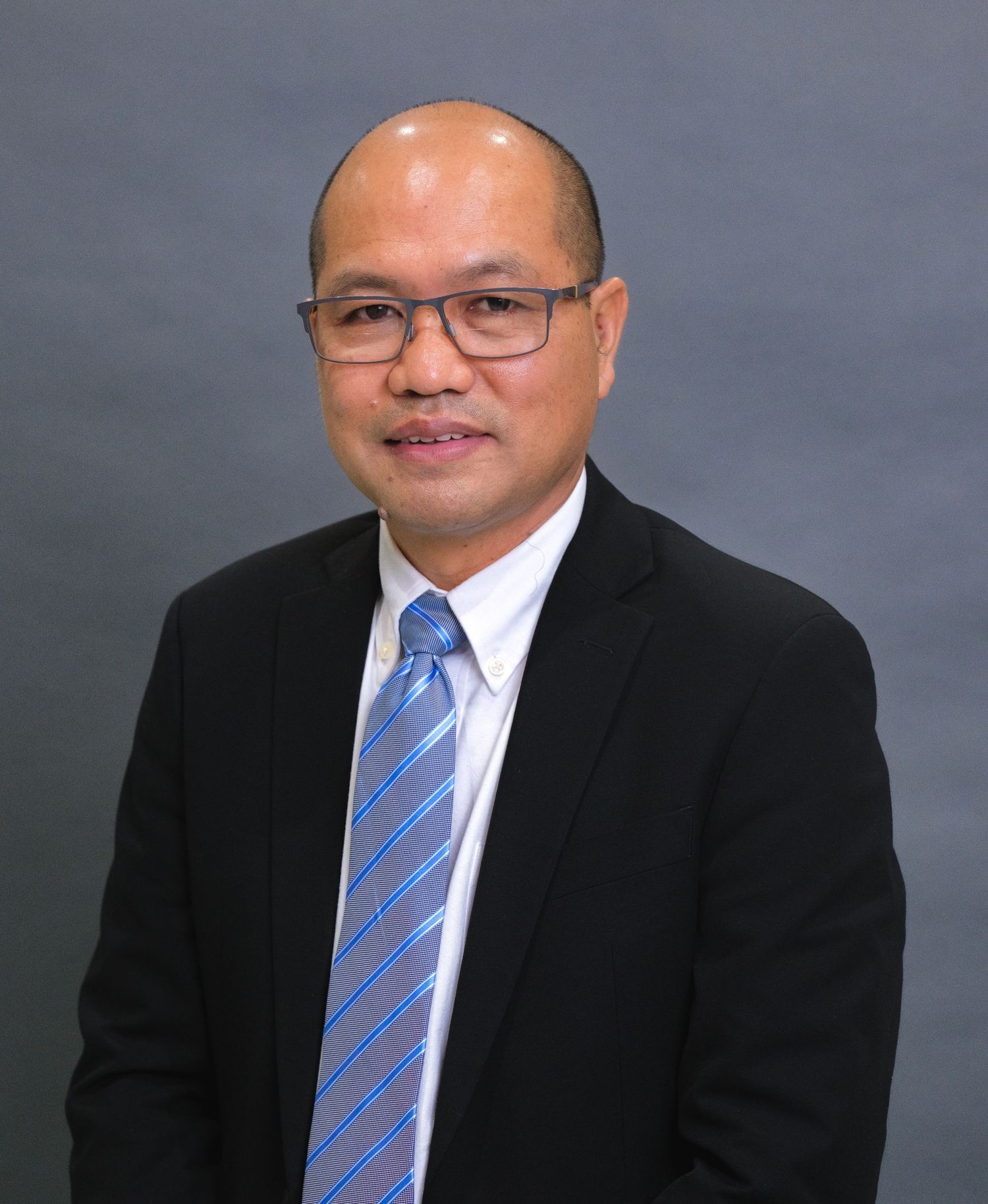 Professional headshot of person in glasses wearing dark suit and striped blue tie against gray background.