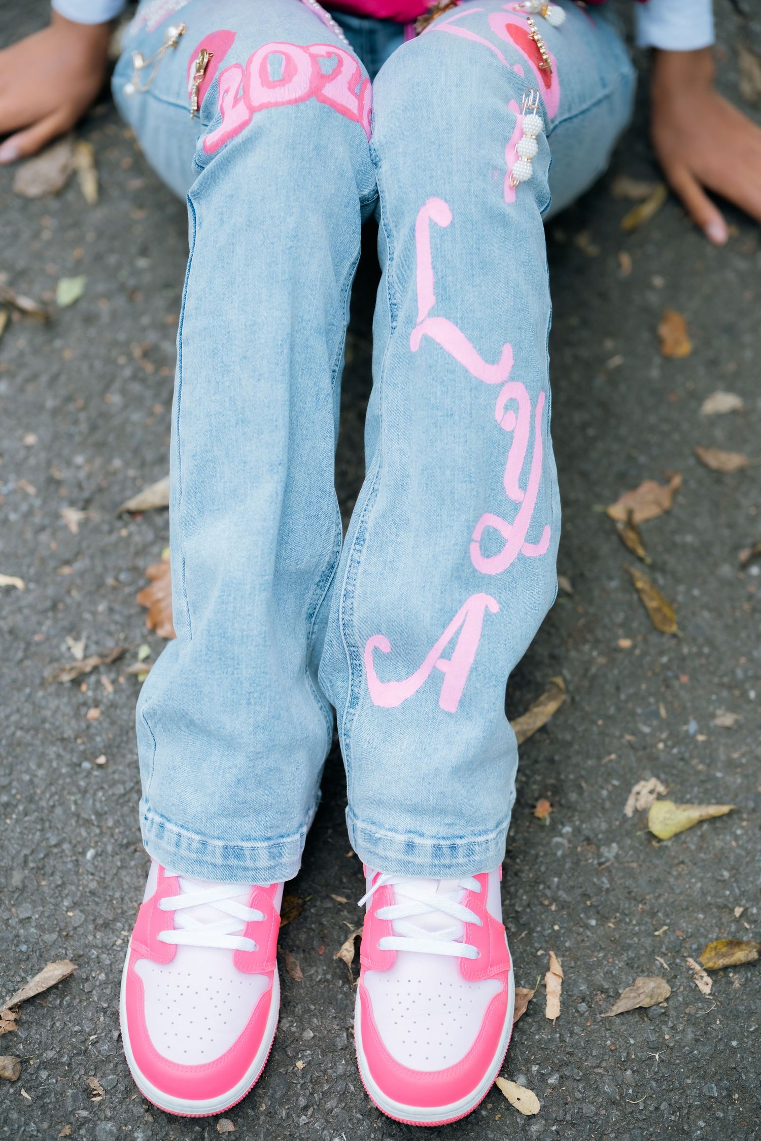 Pink sneakers and decorated denim jeans on a path covered with fallen leaves.