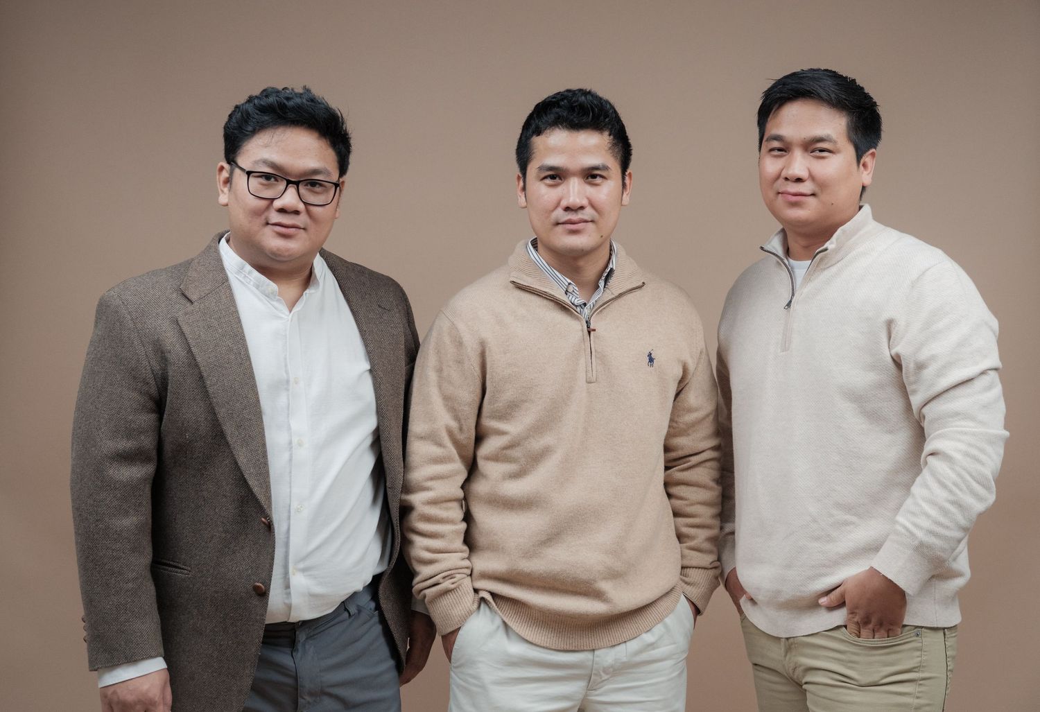 Three people in business casual attire pose against a brown backdrop for a professional photo.