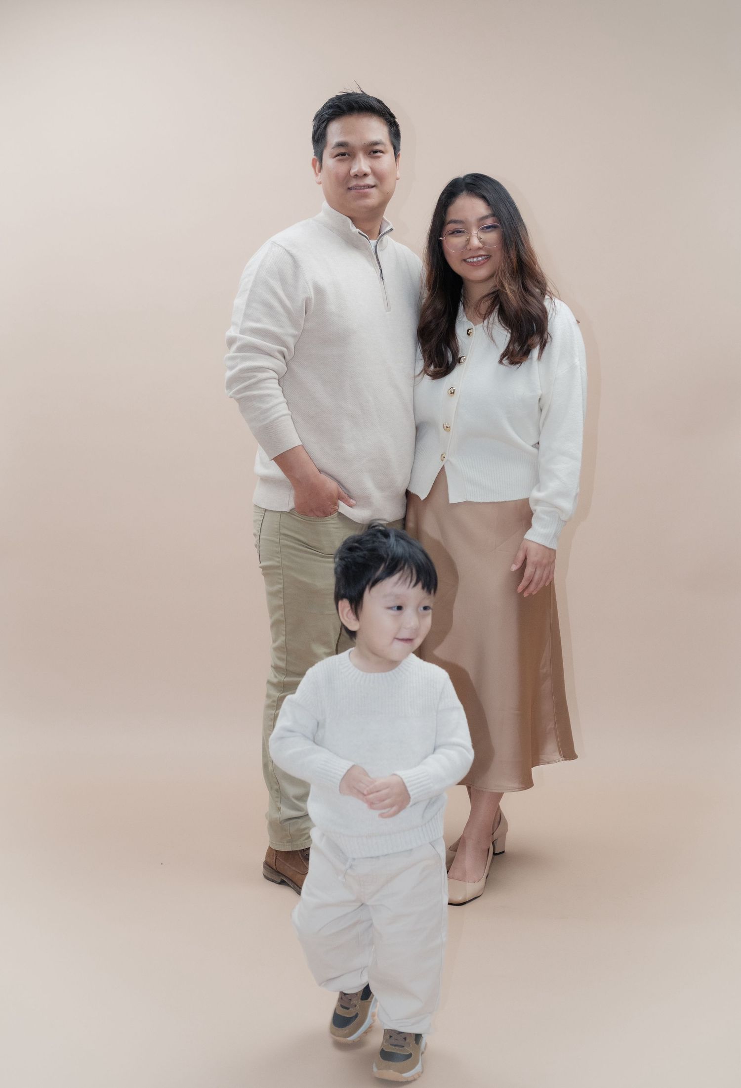 Family in matching white and beige outfits poses for minimalist studio portrait.