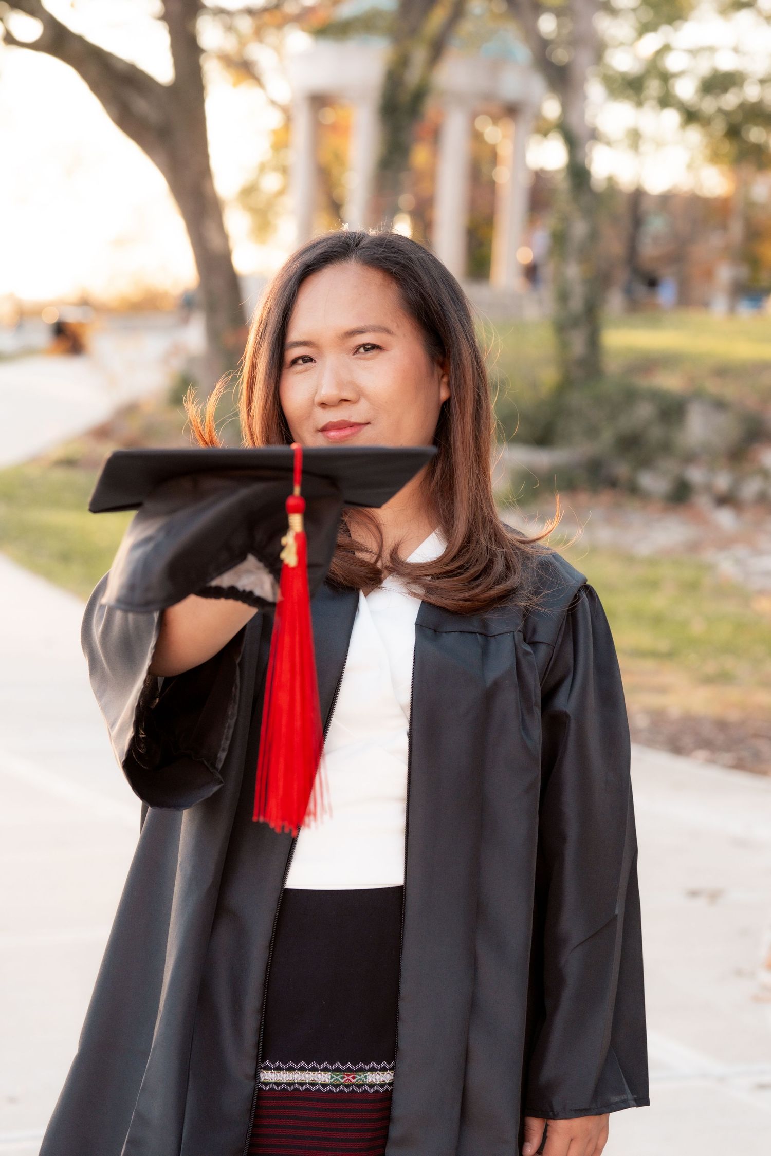 Graduate posing in academic regalia with red tassel against autumn background.