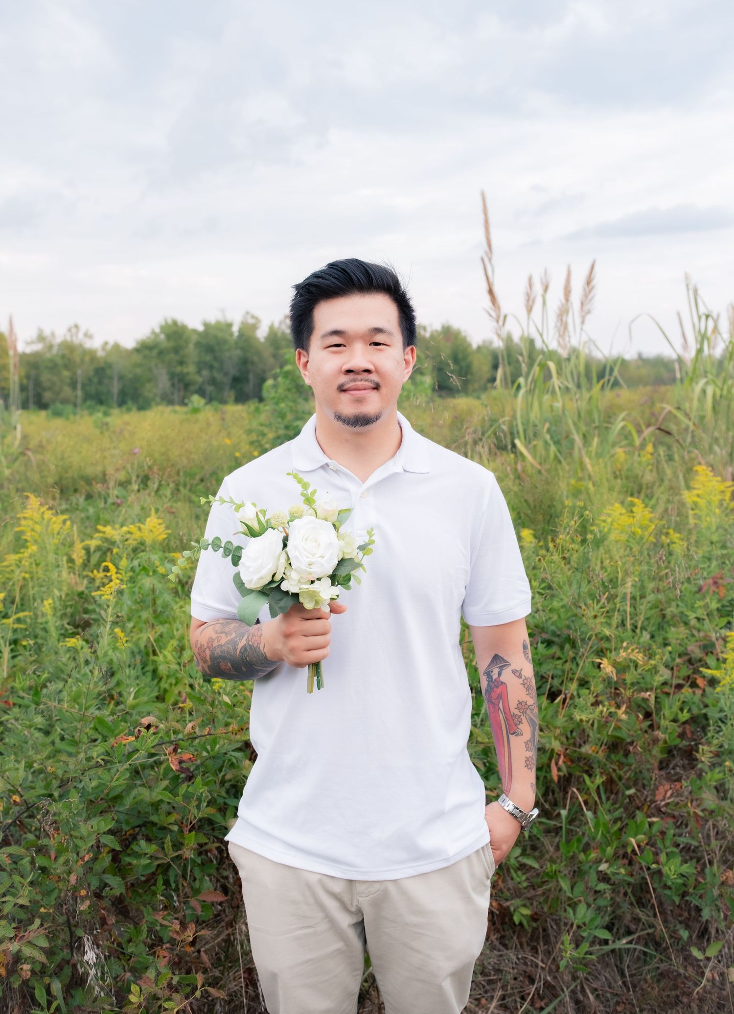 A person in a white polo shirt holds a bouquet of white flowers in a wildflower field.