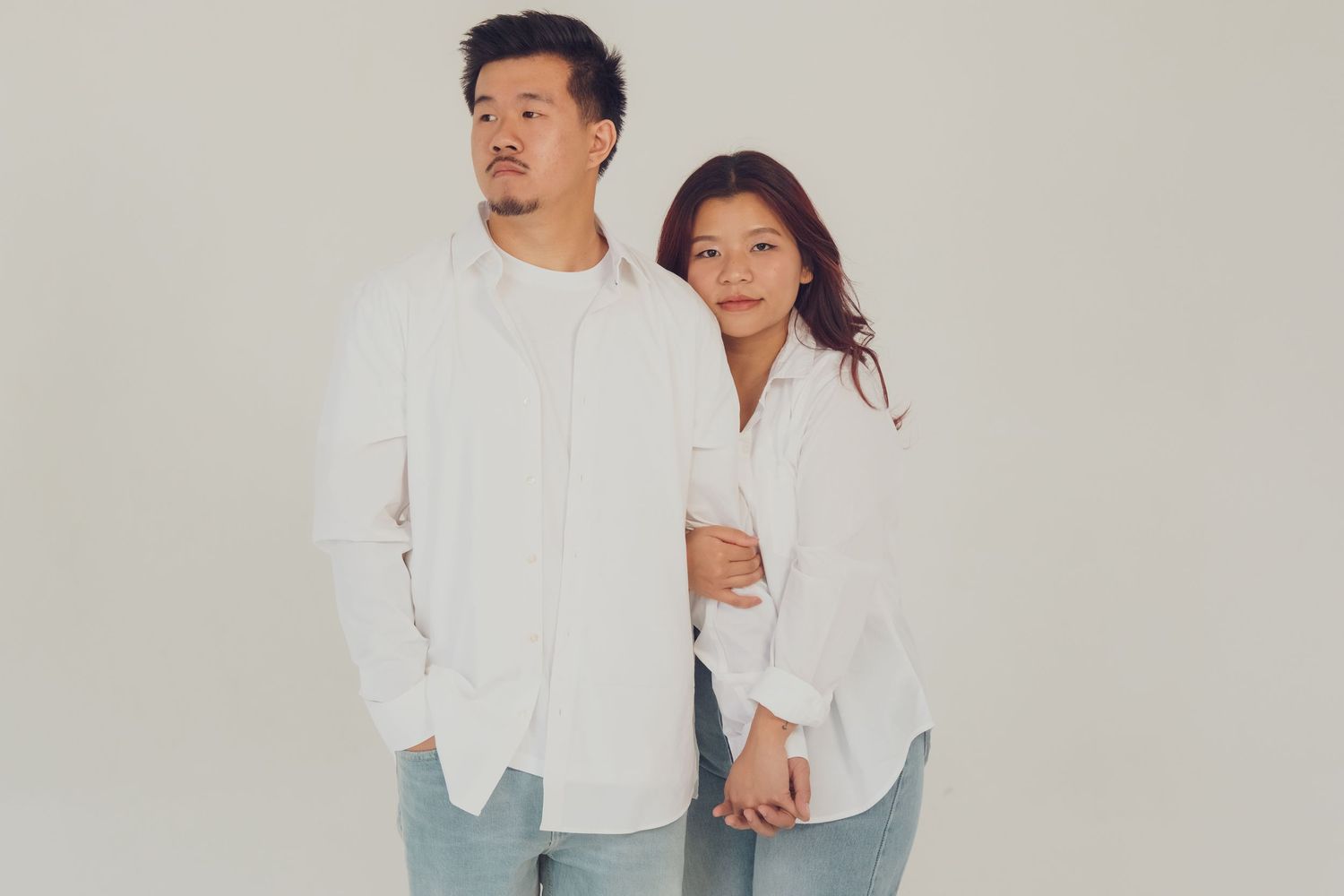 Couple in matching white shirts and jeans pose casually against light background.